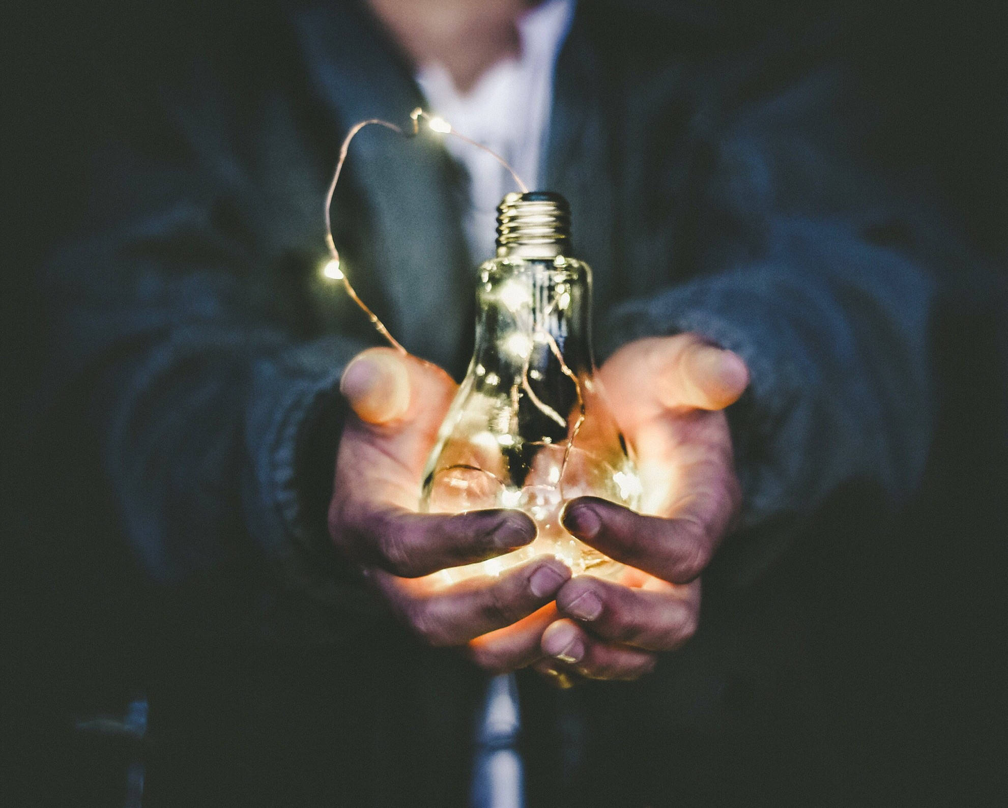 Light Bulb 桌布 壁紙 — 雙手捧著一個發光的燈泡，纏繞著仙女燈，背景黑暗。