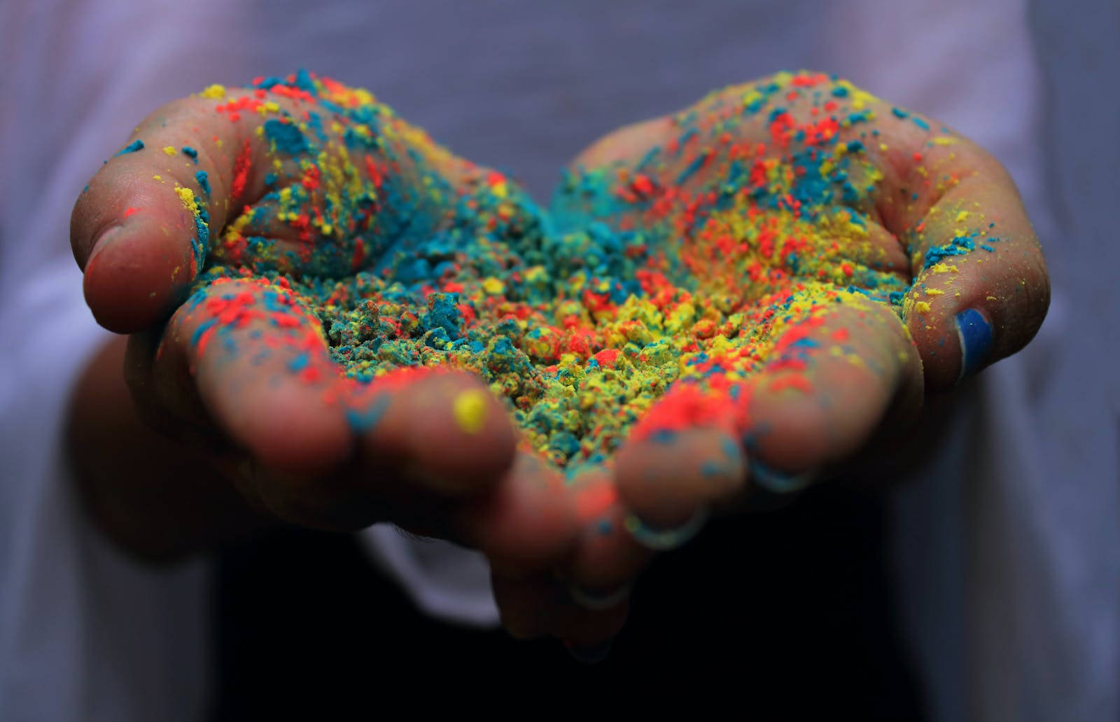 Holi 桌布 壁紙 — 雙手捧著一捧鮮豔的彩虹色粉末，背景柔和模糊。