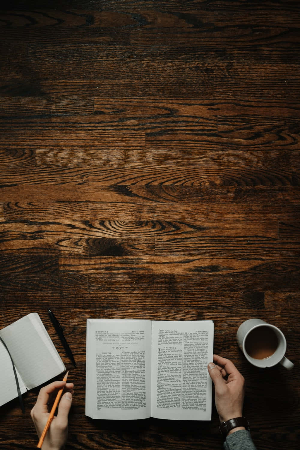 New Testament 桌布 壁紙 — 雙手捧著一本打開的書和鉛筆，旁邊放著一杯咖啡，放在深色木桌上。