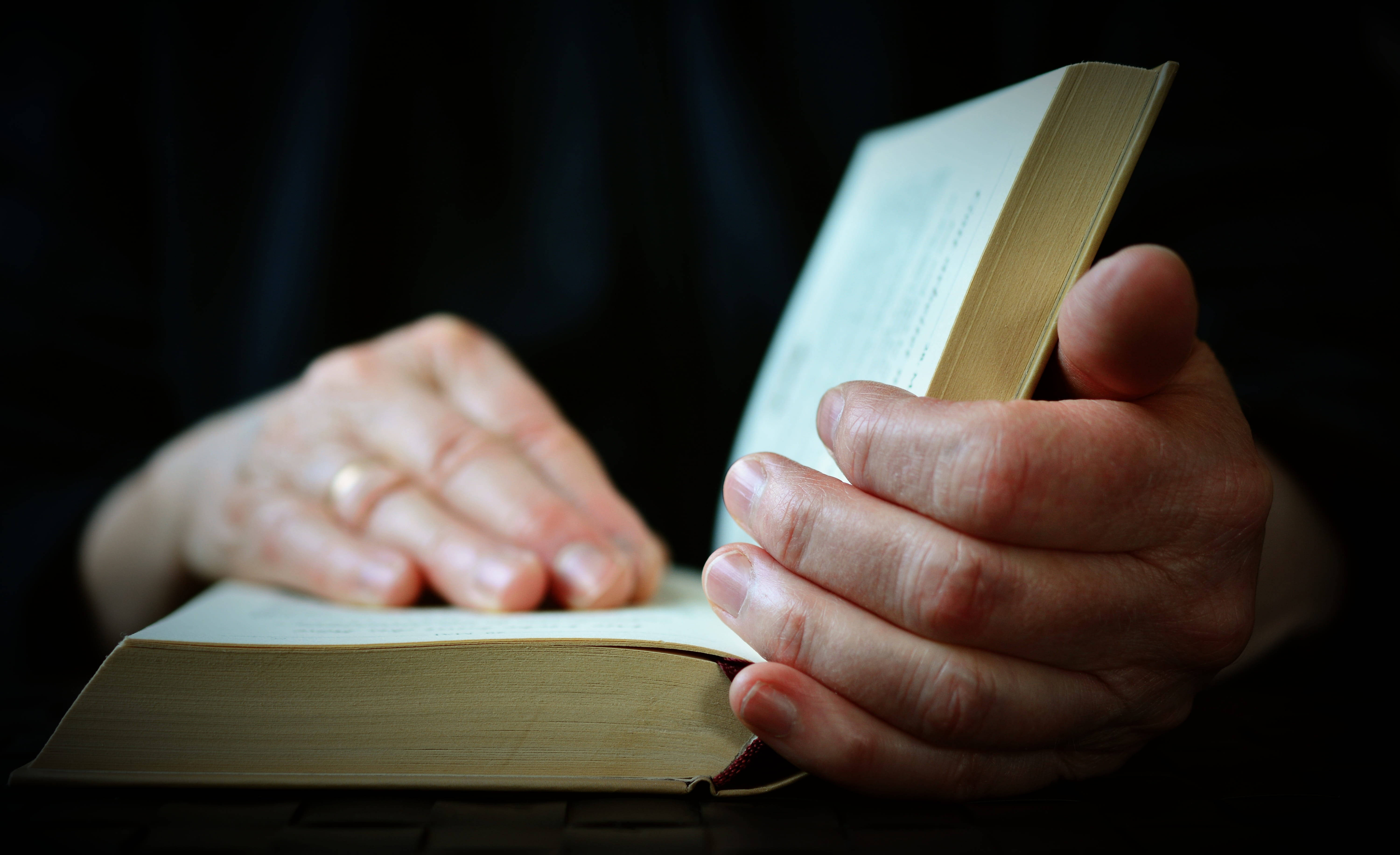 Reading 桌布 壁紙 — 雙手捧著一本打開的書的特寫，柔和光線映襯深色背景。