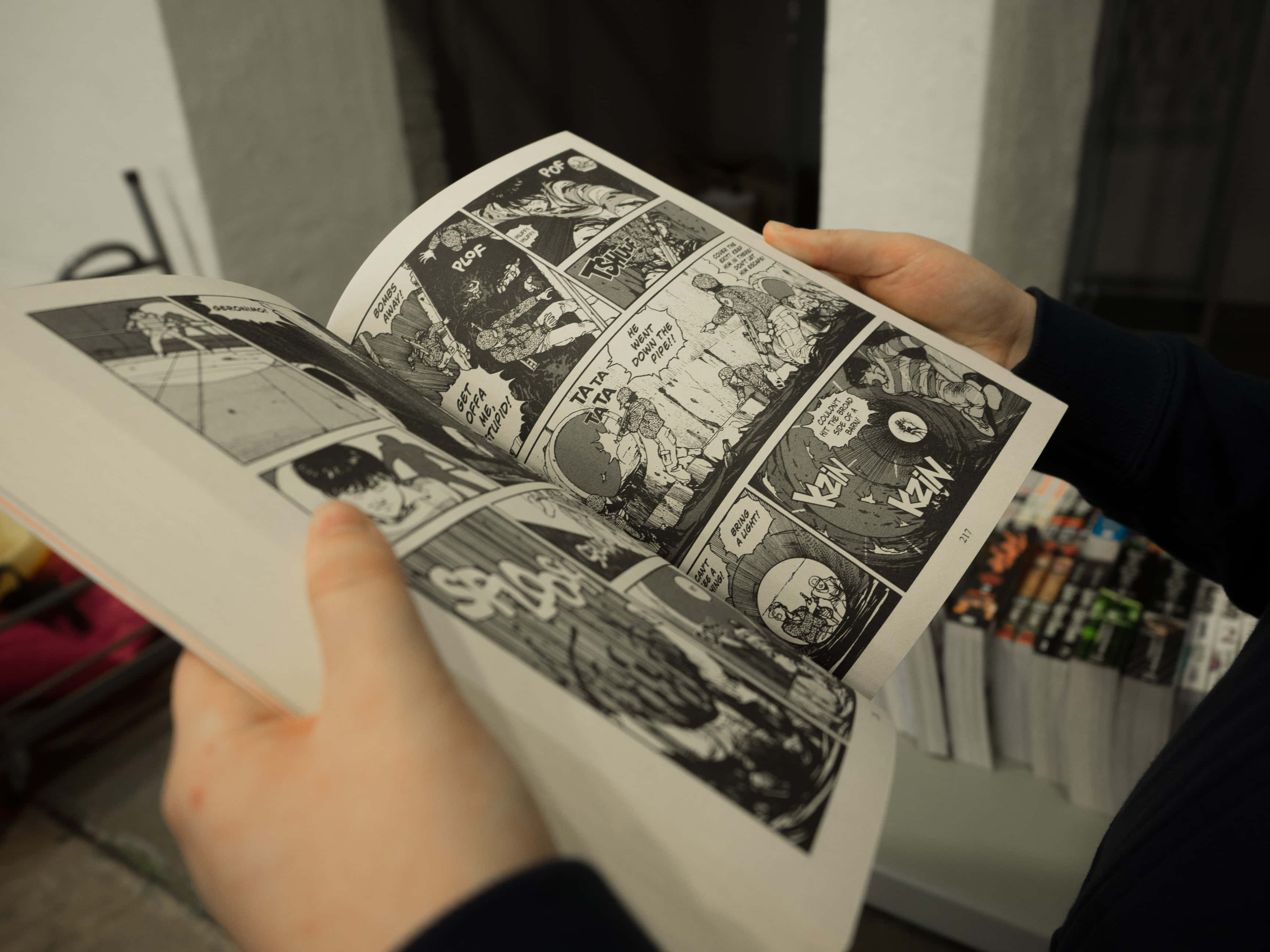 Manga Pages 桌布 壁紙 — 雙手捧著一本打開的漫畫書，顯示動態黑白漫畫格，包含動作場景和對話氣泡。