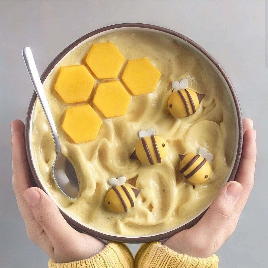 Bee 桌布 壁紙 — 雙手捧著一碗奶油黃色甜點，上面放有蜂巢片和可愛的蜜蜂裝飾。