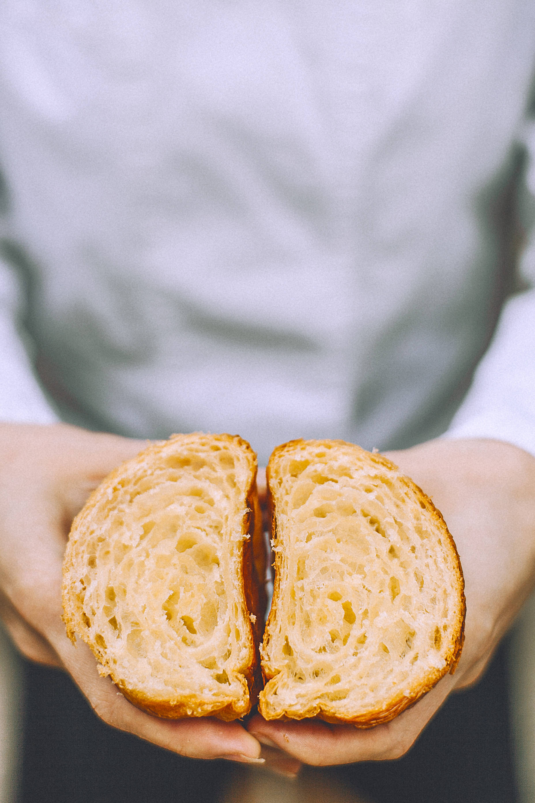 Pastry 桌布 壁紙 — 雙手捧著新鮮出爐的可頌，掰開後露出蓬鬆金黃內層的特寫。