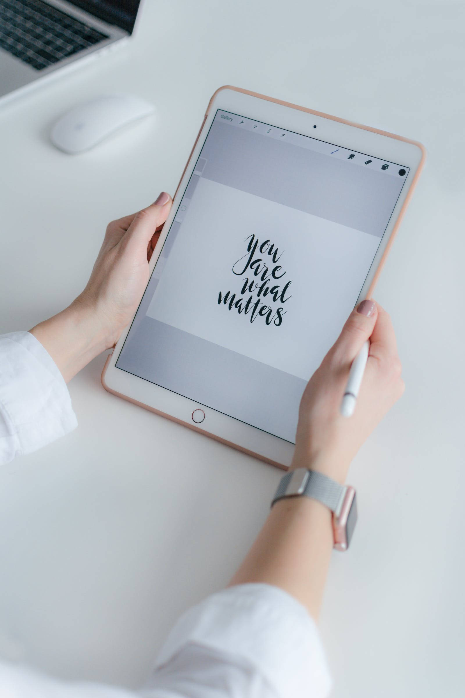 Apple iPad Pro 桌布 壁紙 — 雙手捧著玫瑰金色平板電腦，在簡約白色桌上展示優雅的黑色書法，寫著 you are what matters。