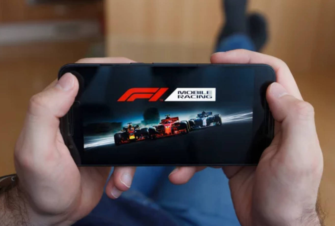 電玩遊戲 桌布 壁紙 — 雙手握住智慧型手機，顯示F1 Mobile Racing遊戲，賽車在賽道上飛馳。
