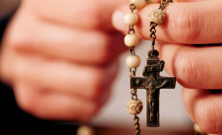 Praying 桌布 壁紙 — 雙手握著帶有精細十字架的玫瑰經念珠的特寫，背景柔和模糊。