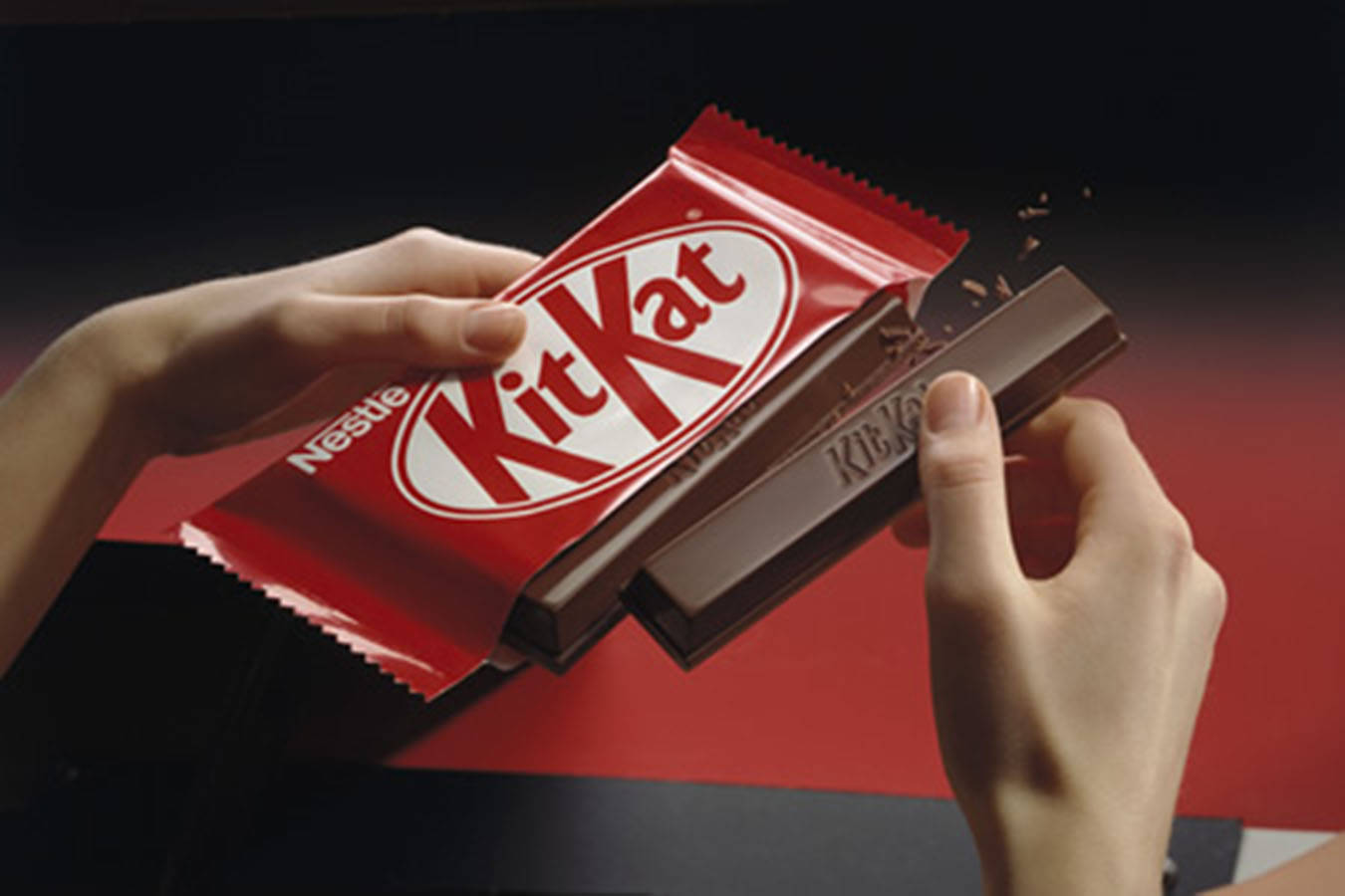 Chocolate 桌布 壁紙 — 雙手撕開紅色KitKat包裝，露出巧克力棒，脆脆的威化層正在碎裂。