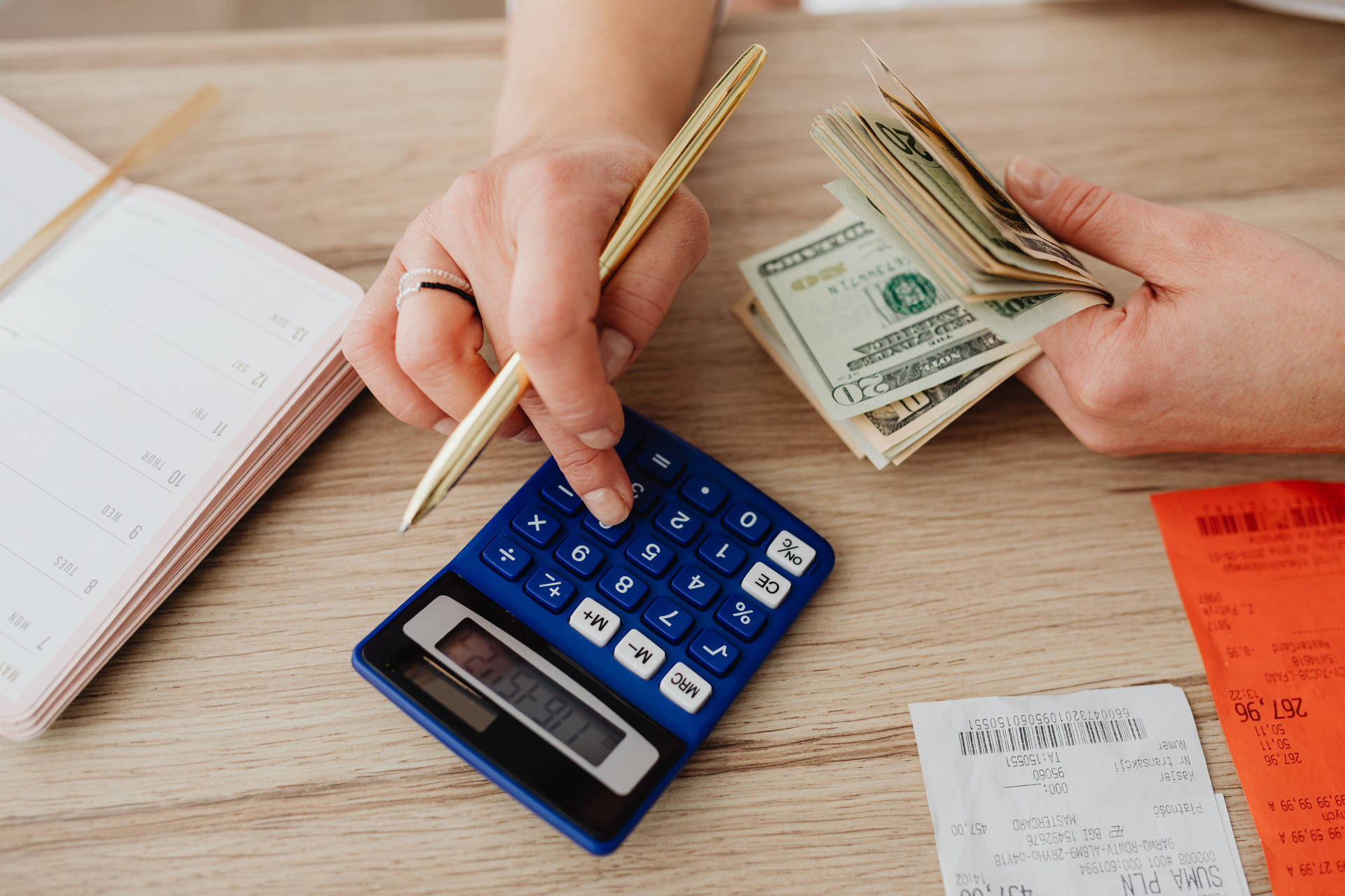 人在木桌上用現金和計算機計算開支。