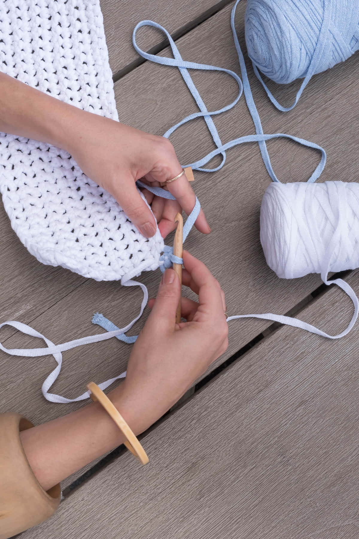 Crocheting 桌布 壁紙 — 雙手熟練地在風化的木甲板上用淺藍色紗線鉤織白色織物。
