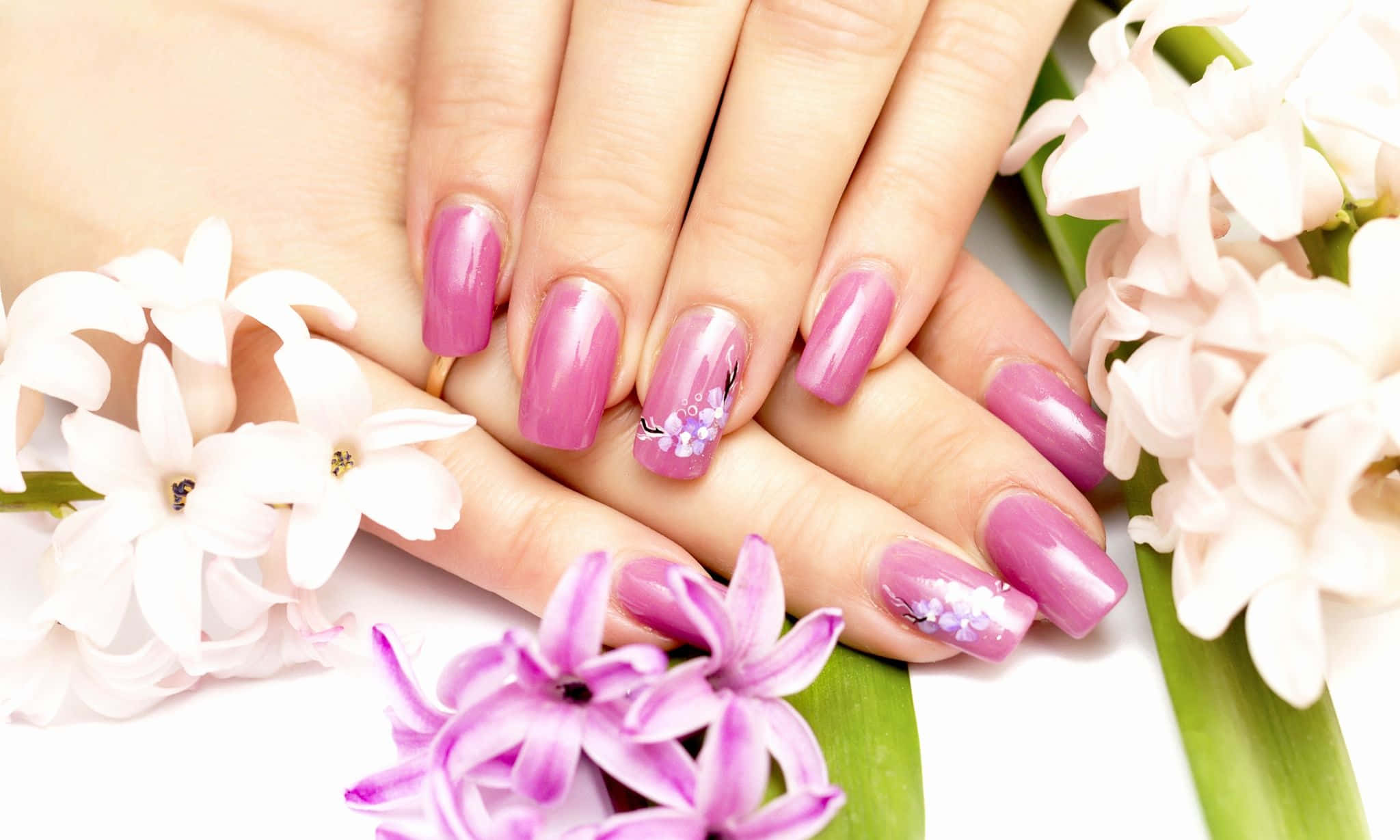 Pink Nails 桌布 壁紙 — 雙手特寫，帶有光澤的粉紅色指甲，飾有精緻的花卉圖案，周圍環繞著新鮮的白色和紫色風信子。