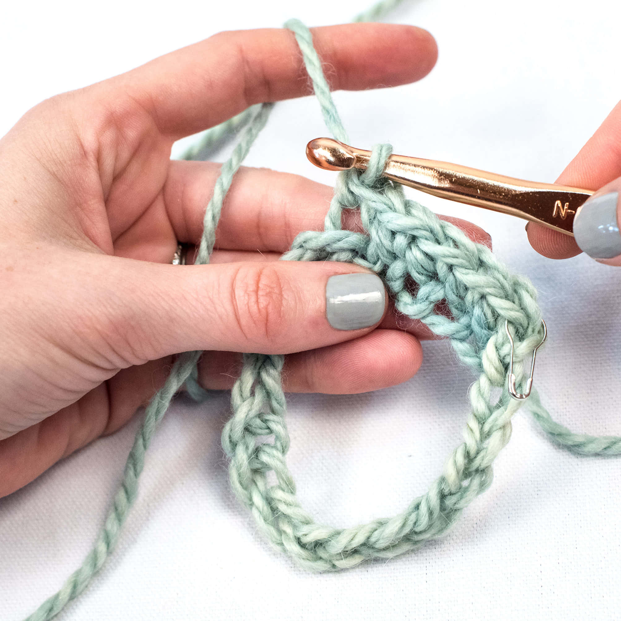 Crocheting 桌布 壁紙 — 雙手用玫瑰金鉤針編織淺綠色毛線的特寫，背景為白色。