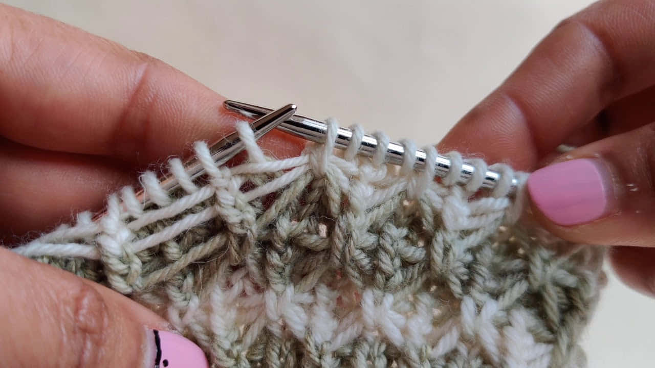 Butterfly Stitch 桌布 壁紙 — 雙手用銀色織針和粉紅色指甲油編織有紋理布料的特寫。