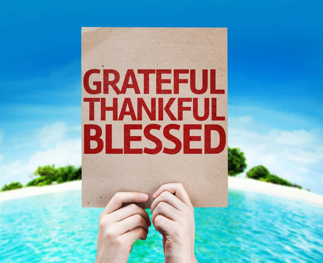 Thankful 桌布 壁紙 — 雙手舉起一個紙板標語，上面用紅色文字寫著「感恩感恩祝福」，背景是熱帶海灘。