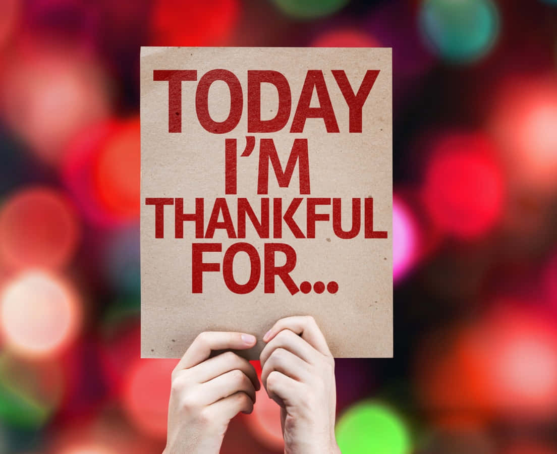 Thankful 桌布 壁紙 — 雙手舉起一塊紙板，上面寫著「今天我感恩的是……」，背景是色彩繽紛的散景。