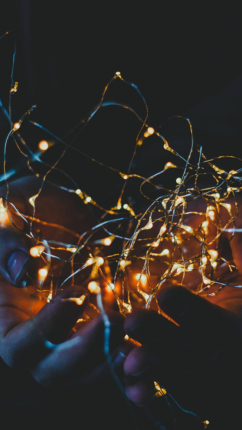Fairy Lights Aesthetic 桌布 壁紙 — 雙手輕輕捧著一團溫暖發光的童話燈，背景漆黑。