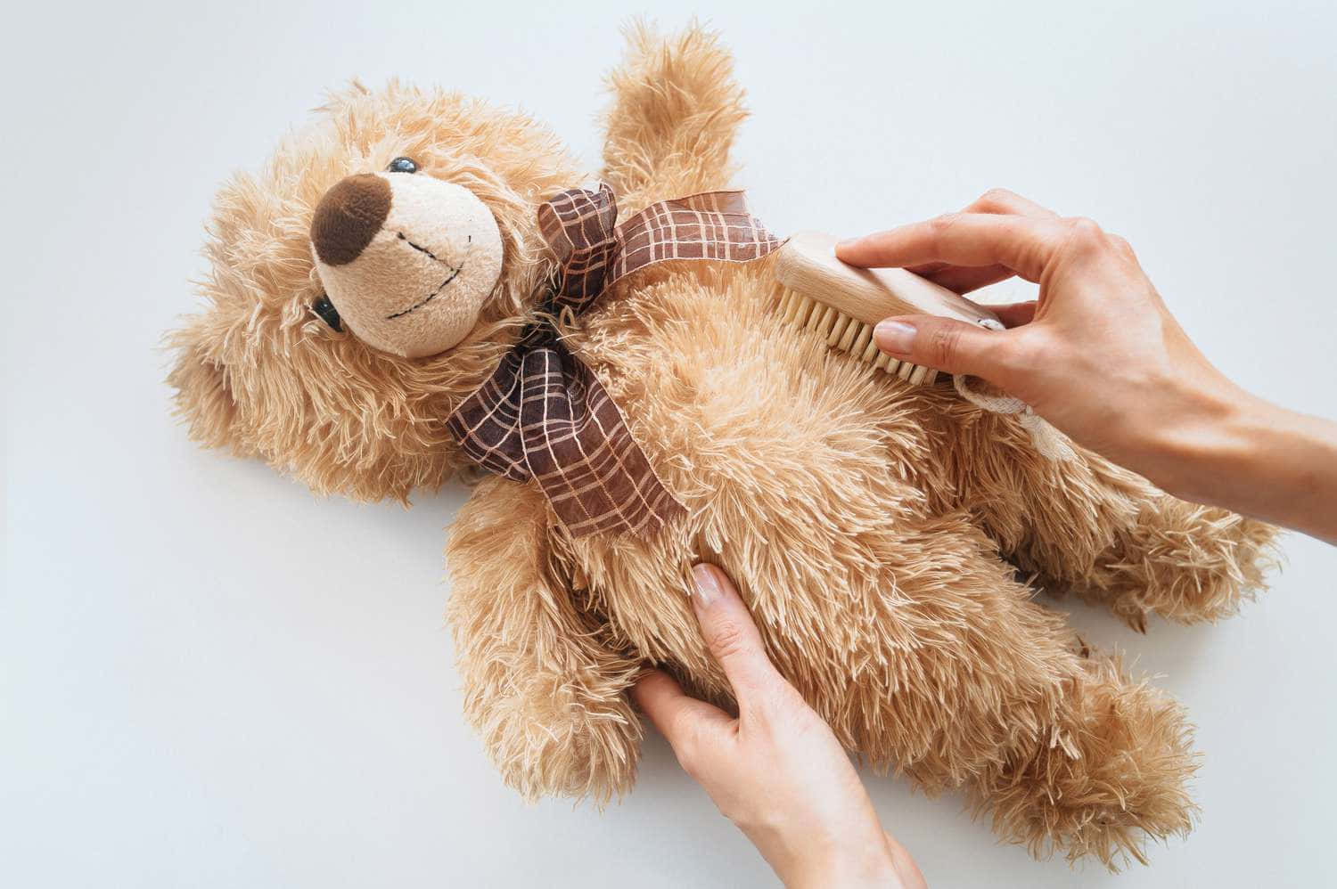 Teddy Bear 桌布 壁紙 — 雙手輕輕撫摸一隻戴著格紋蝴蝶結的棕色泰迪熊的蓬鬆毛髮，背景是純白色。