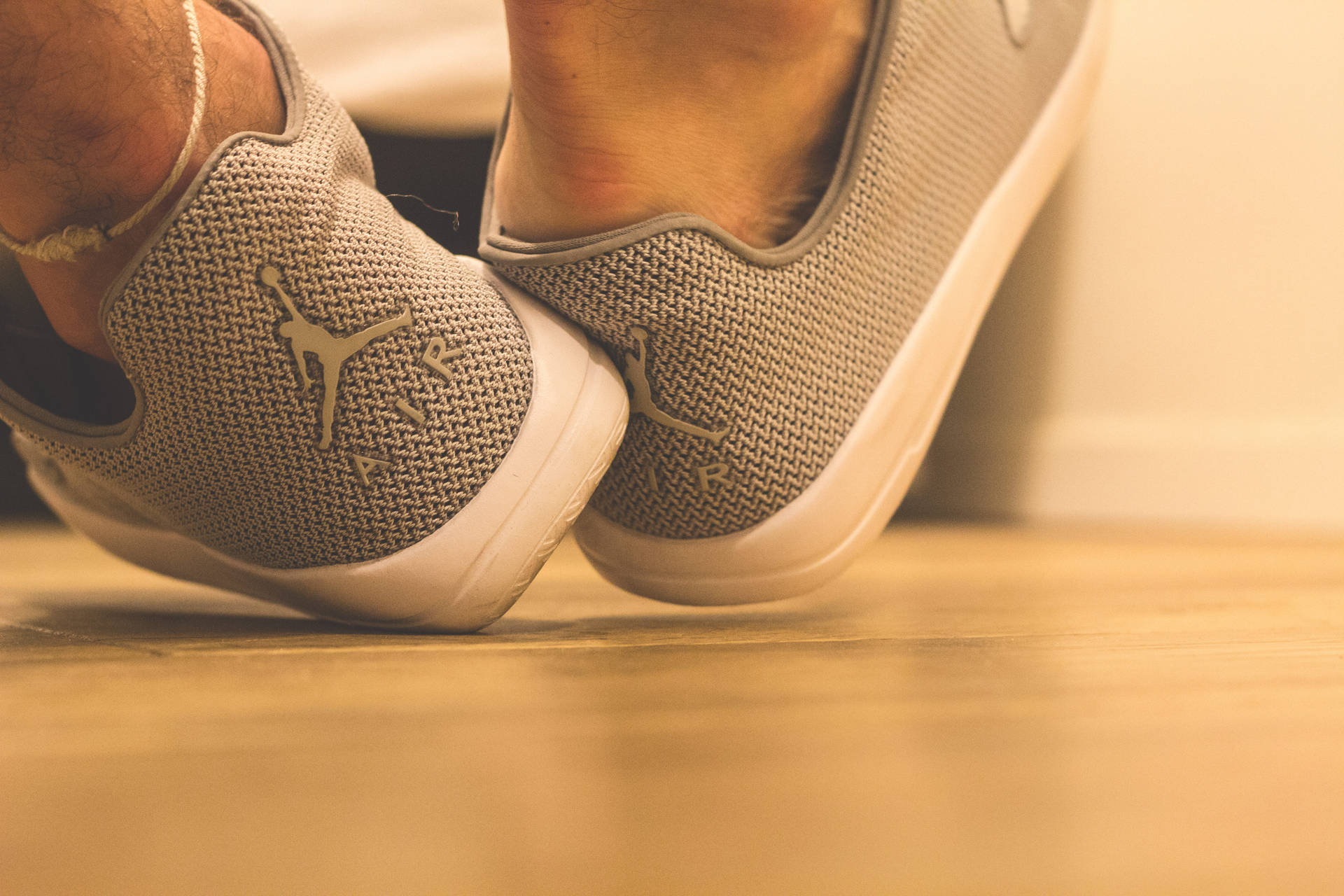 雙腳穿著灰色套入式運動鞋，帶有Jumpman標誌，在木地板上。 — Air Jordan 1 壁紙