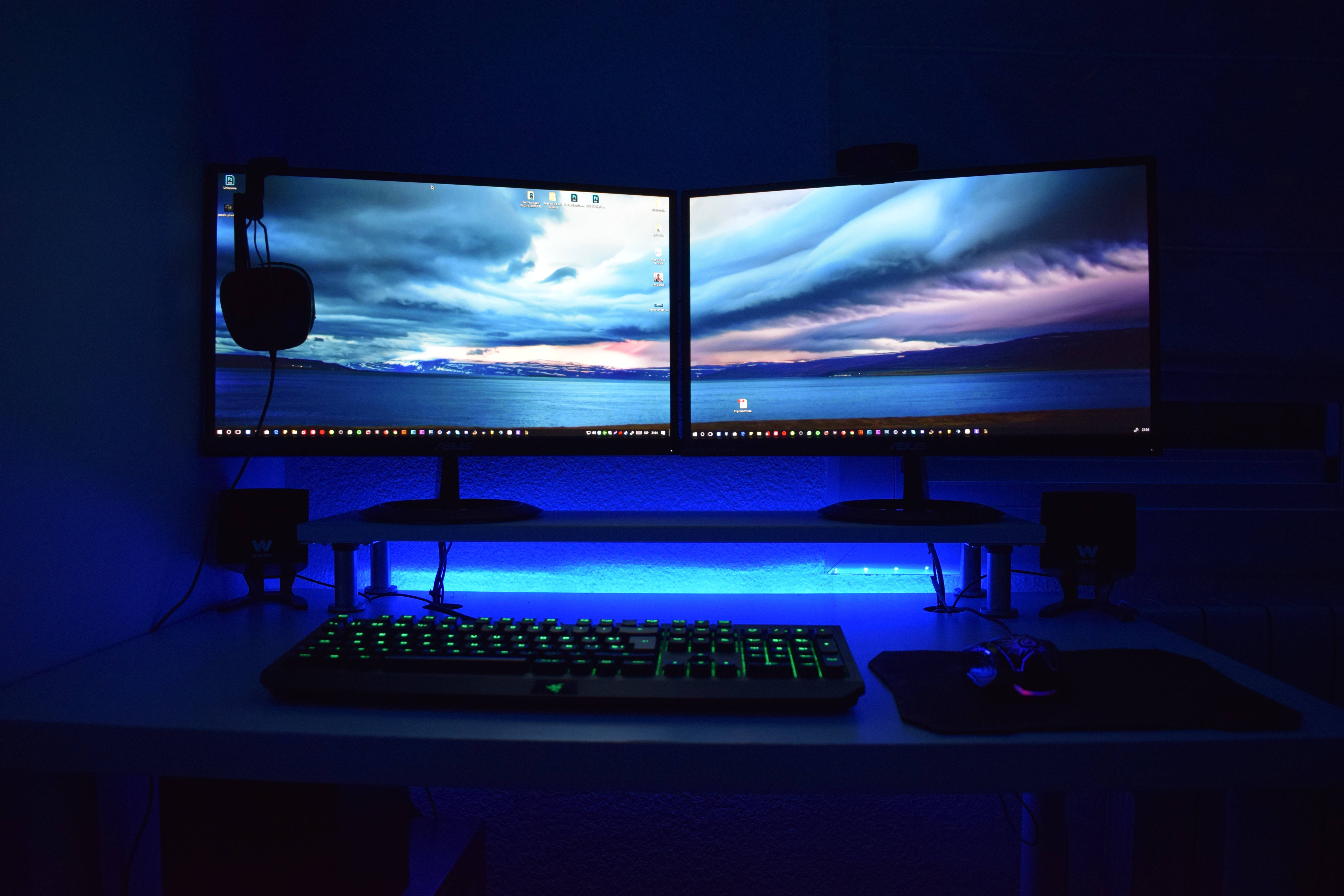 Desk 桌布 壁紙 — 雙顯示器遊戲設置，沐浴在藍光中，在黑暗的環境燈光下，鍵盤和滑鼠發光。