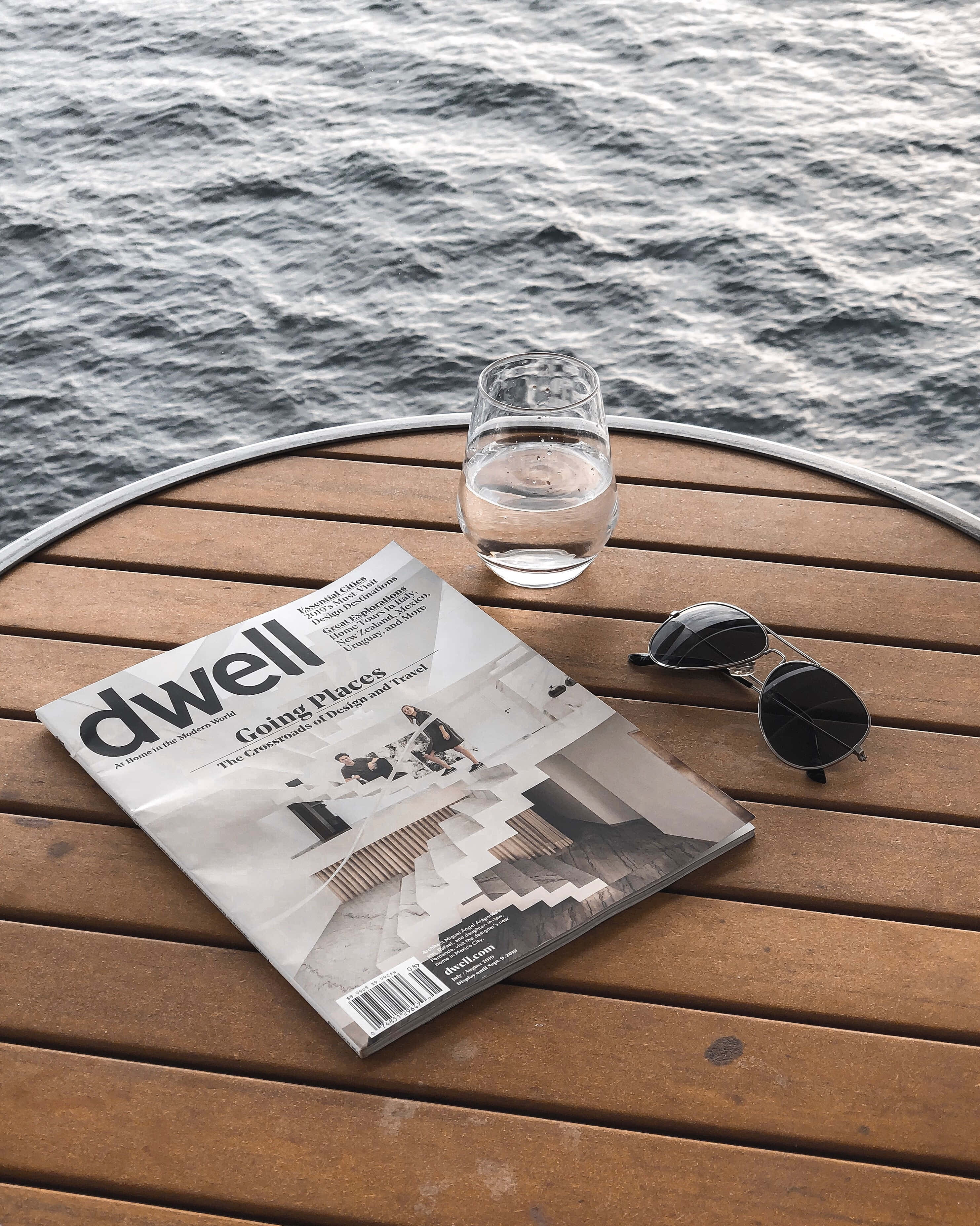 雜誌 桌布 壁紙 — 雜誌杯和太陽眼鏡放在木甲板上，俯瞰漣漪的水面。