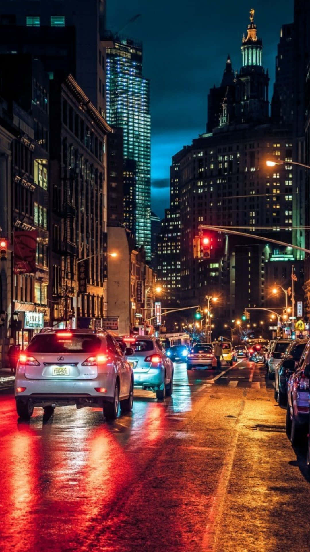 Android Ny City 桌布 壁紙 — 雨夜中濕滑的城市街道，在 towering 的燈火通明摩天大樓下，汽車尾燈在濕漉漉的路面上反射出光芒。