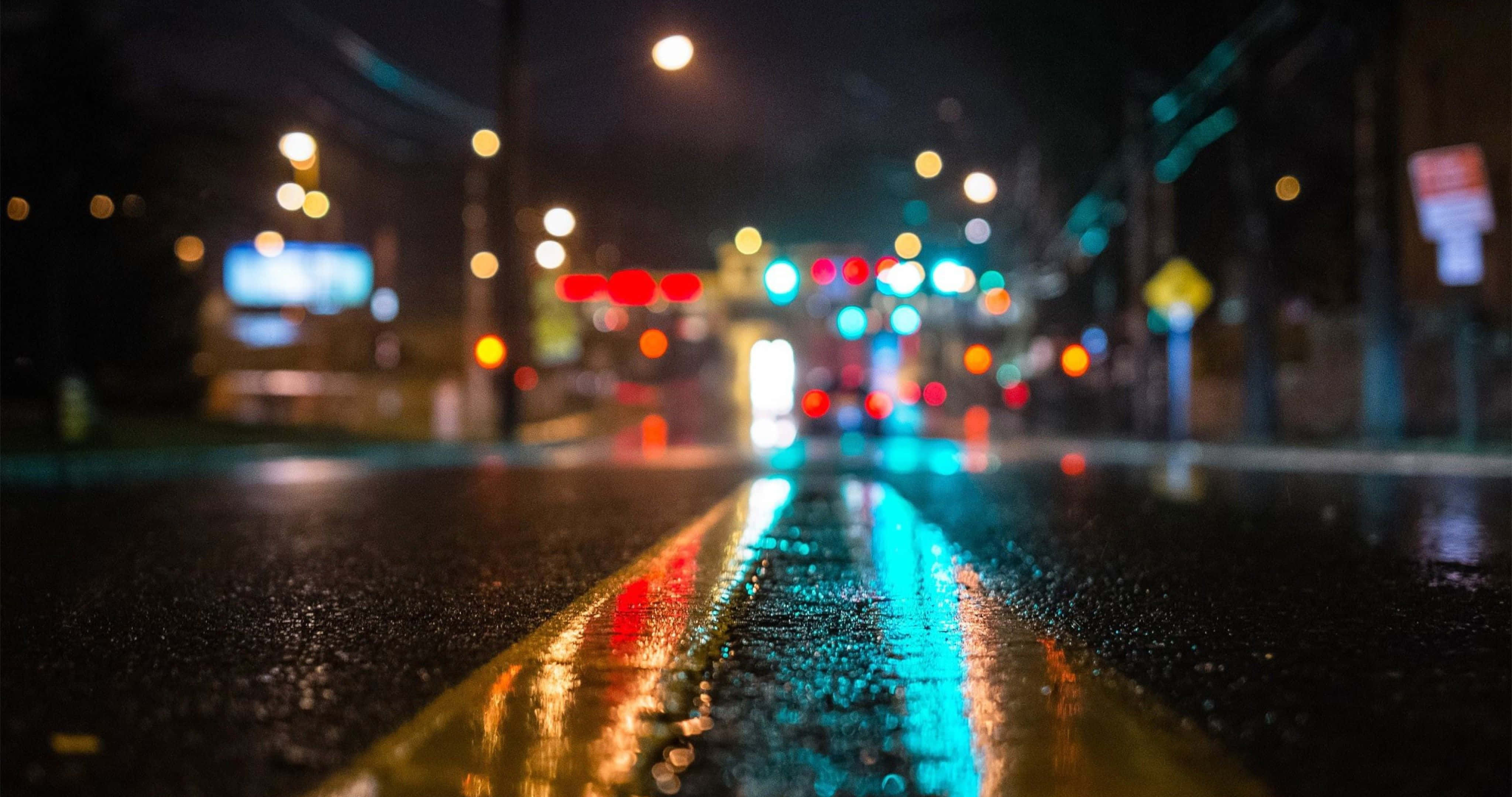 4K Desktop Pc 桌布 壁紙 — 雨夜中濕滑的城市街道，發光的散景燈光反射在濕漉漉的瀝青和黃色中心線上。