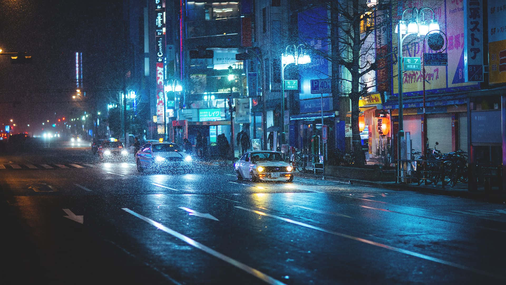 Rainy 桌布 壁紙 — 雨夜中濕滑的城市街道，發光的霓虹招牌倒映在濕漉漉的路面上，汽車在傾盆大雨中行駛。