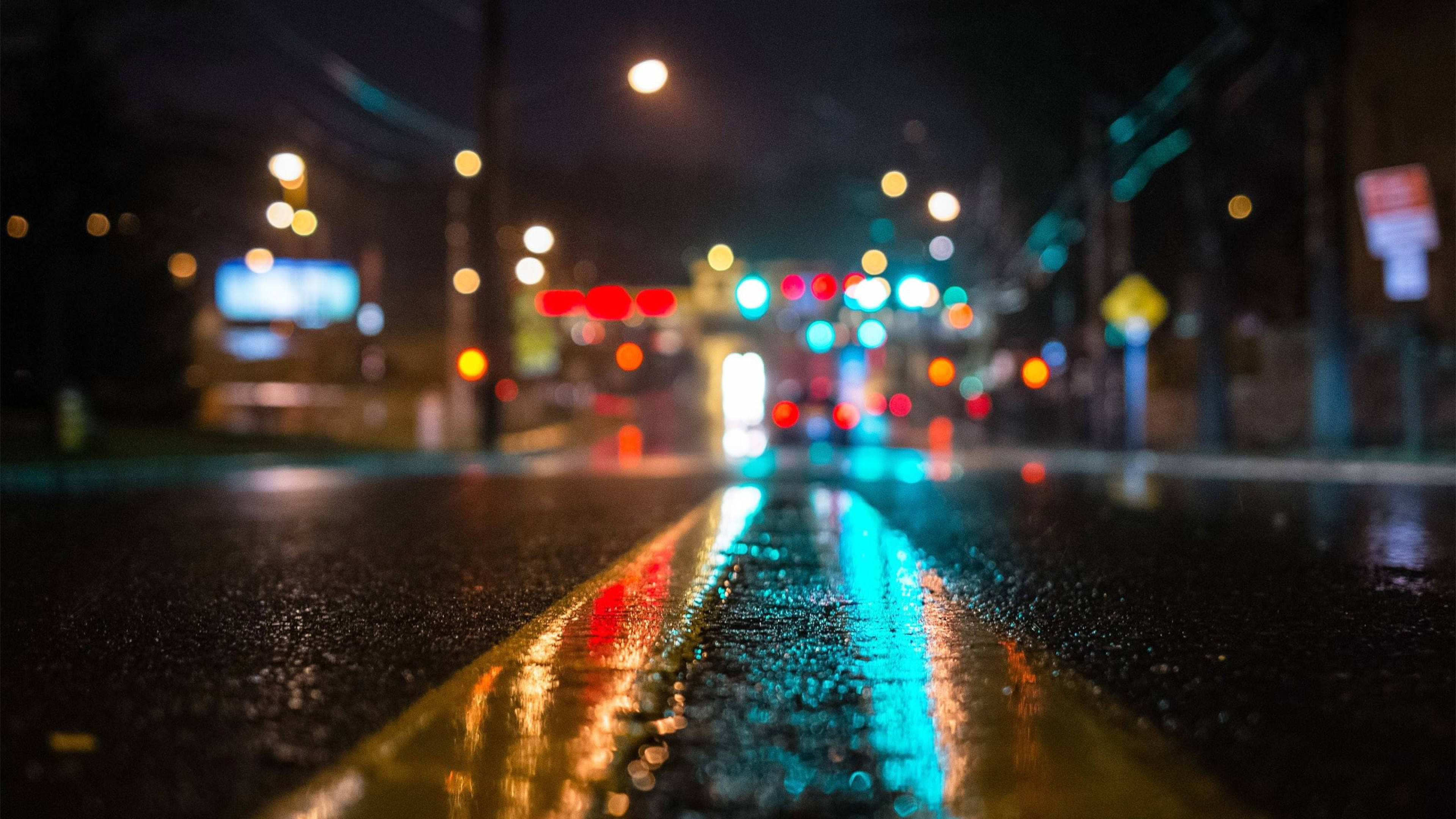 4K Pc 桌布 壁紙 — 雨夜中的城市街道，潮濕的瀝青路面和黃色中心線上反射著發光的散景燈光。