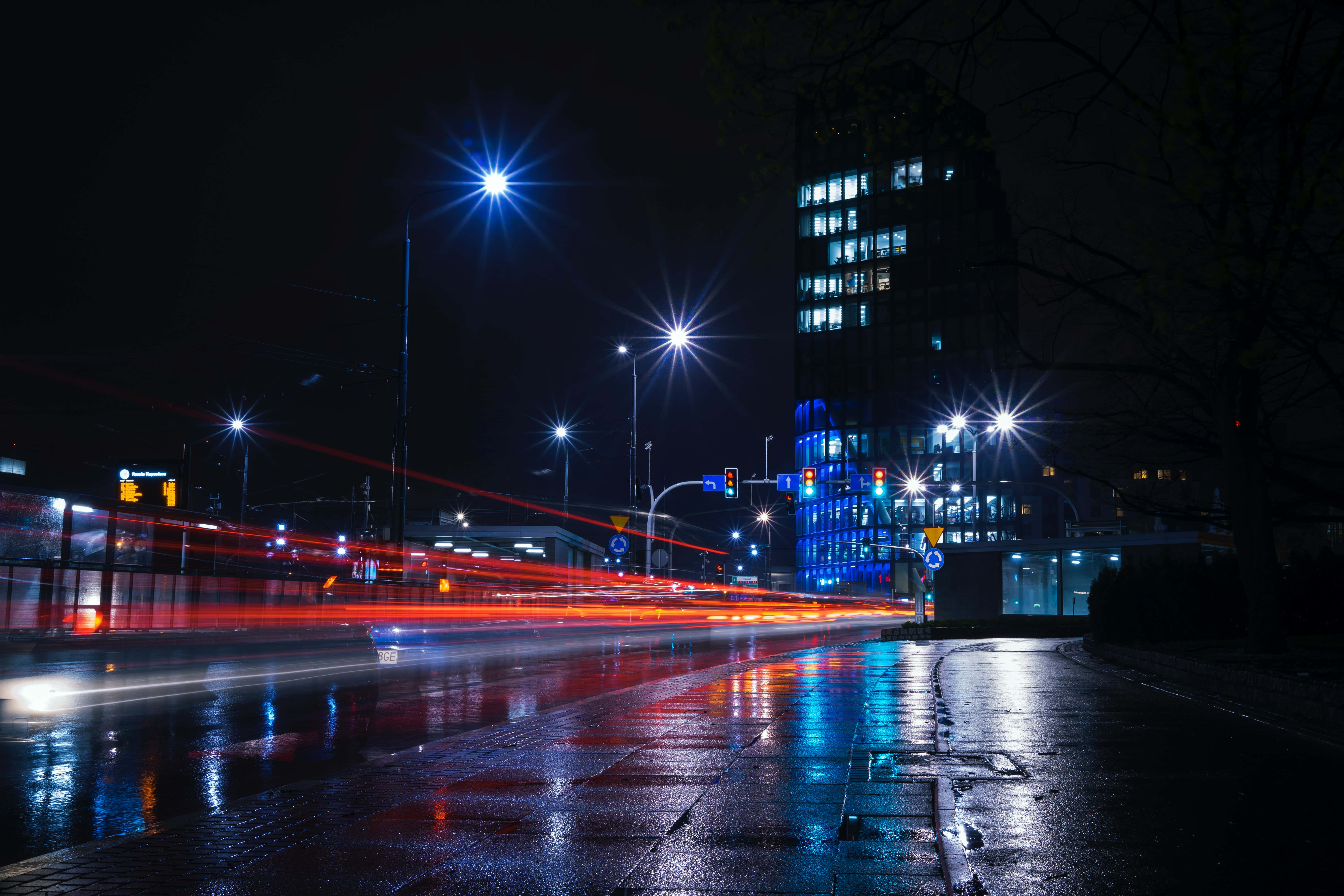 Night Street 桌布 壁紙 — 雨夜城市景觀，發光的街燈和紅色車燈的條紋在潮濕的路面上反射。