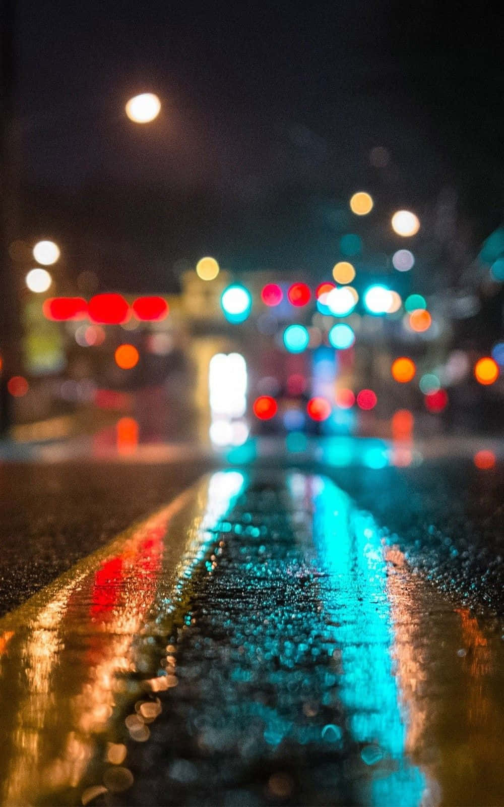 iPhone 桌布 壁紙 — 雨夜濕滑的城市街道，發光的散景燈光在濕漉漉的瀝青上反射。