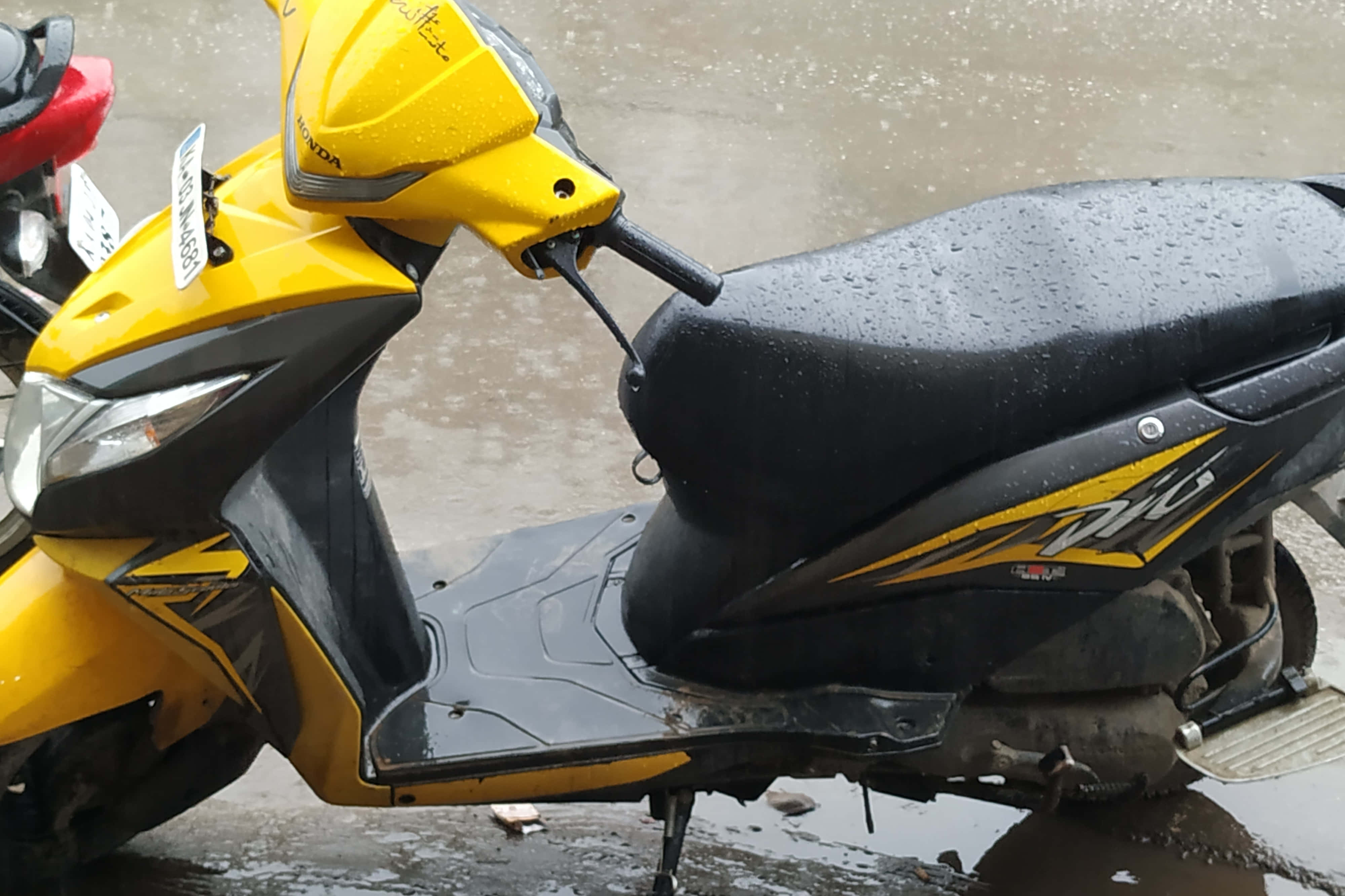 機車 桌布 壁紙 — 雨後一輛亮黃色本田機車配黑色座椅停在濕漉漉的路面上，表面水珠閃閃發光。