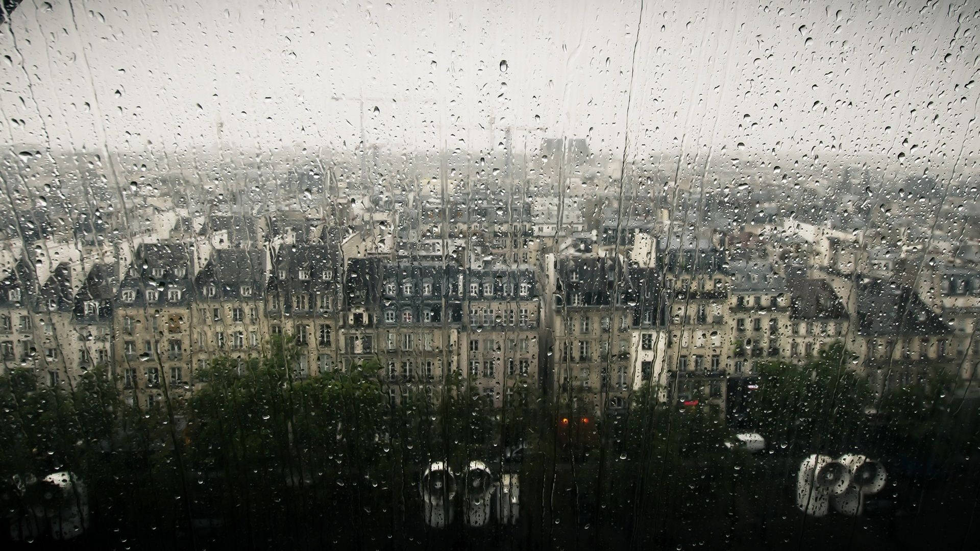 Raining 桌布 壁紙 — 雨水沿窗戶流下，顯露出灰色天空下歐式建築的迷濛城市天際線。