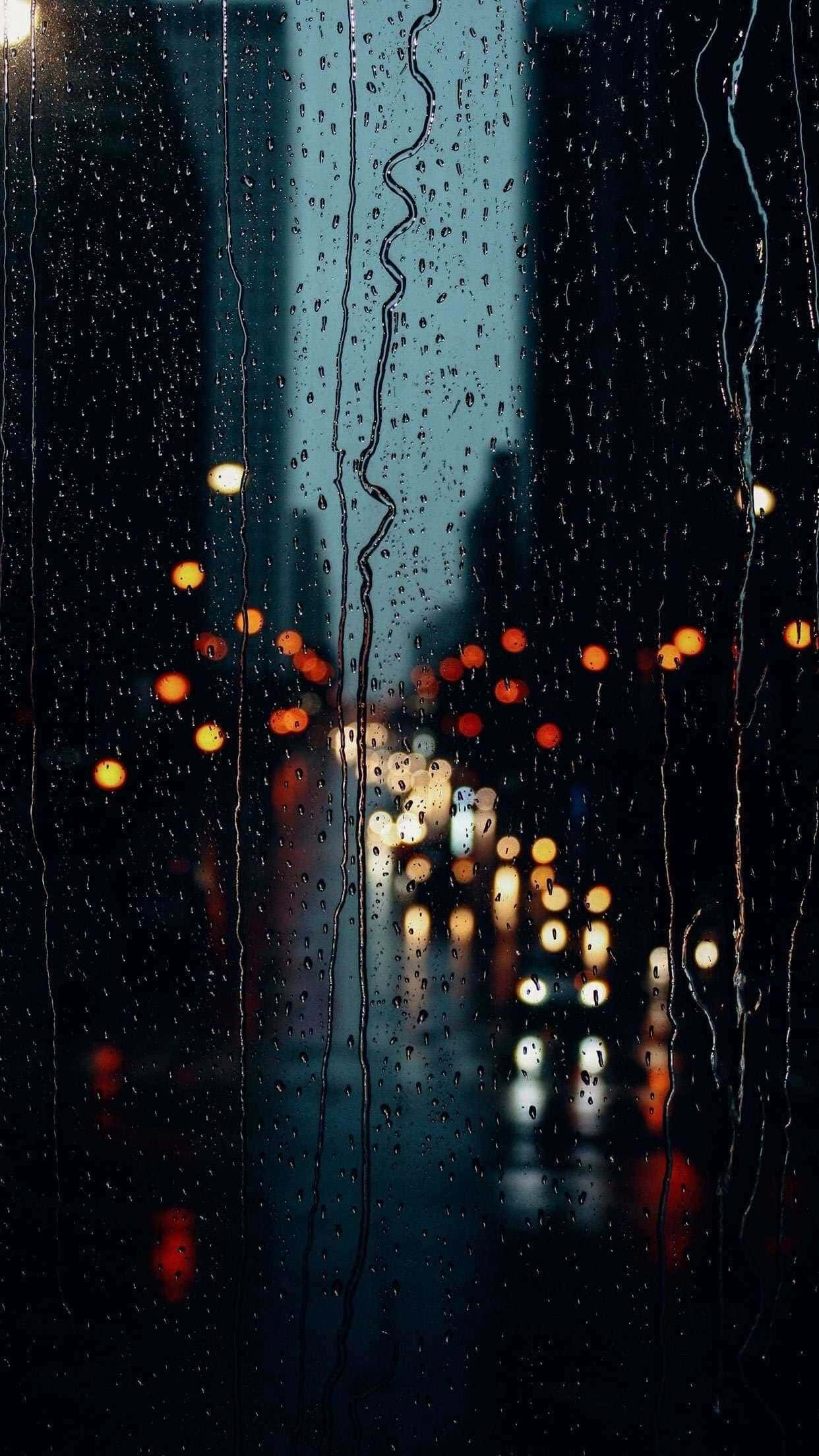 下雨 桌布 壁紙 — 雨水沿窗流下，將城市燈光模糊成溫暖發光的光球，映襯著漆黑的夜晚。