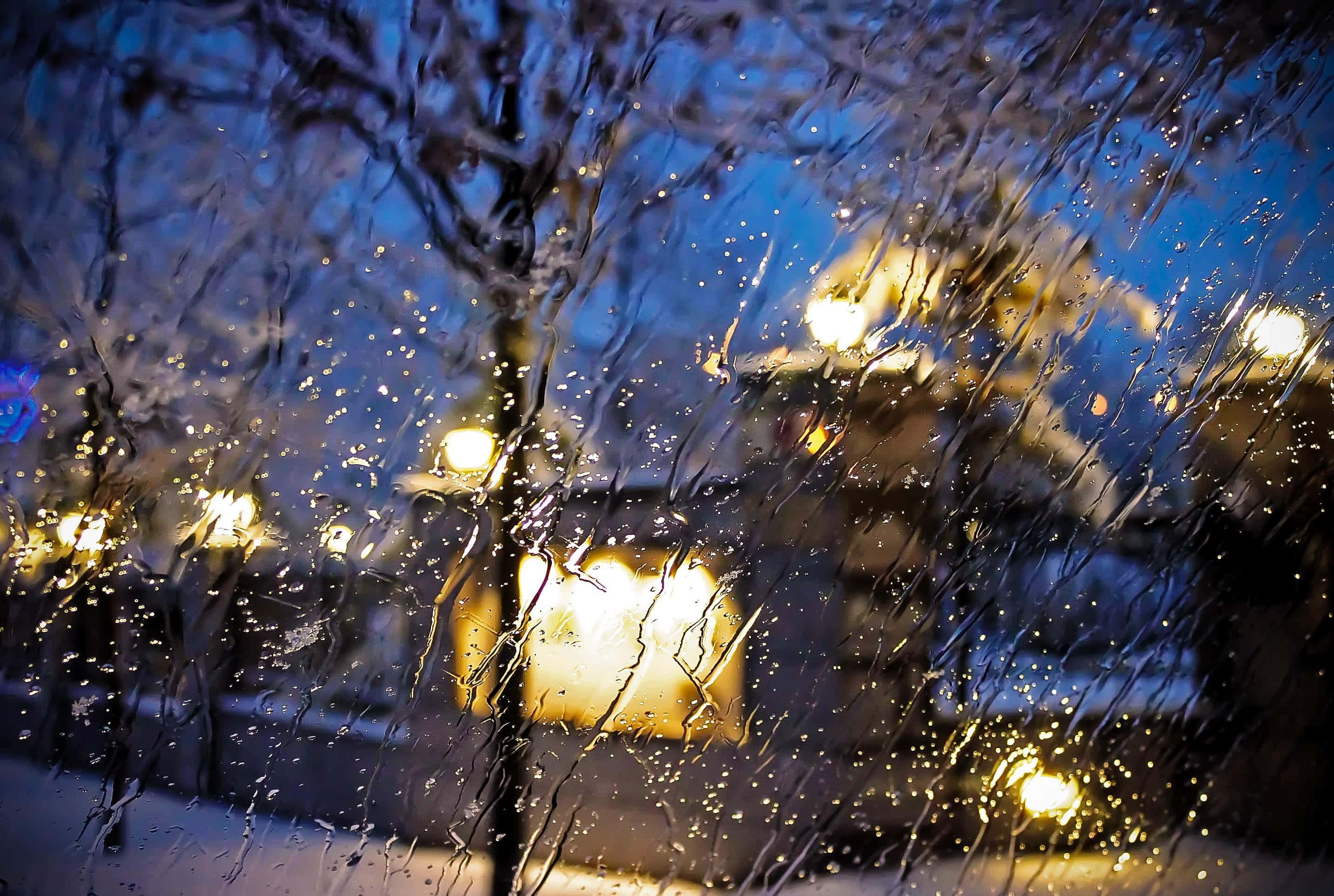 Raining 桌布 壁紙 — 雨水沿窗流下，顯現模糊的街燈和積雪的樹木，映襯著暮藍色的天空。