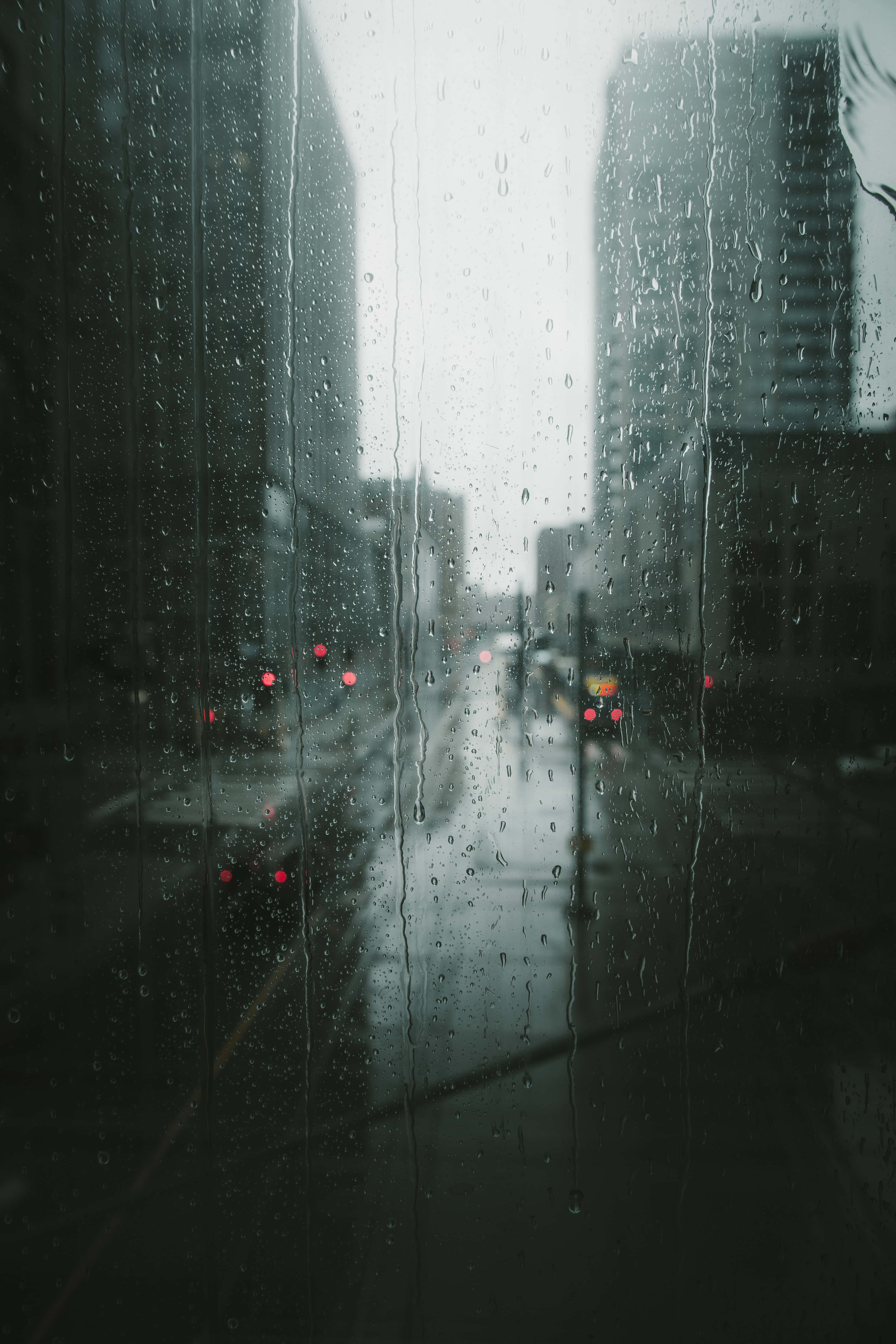 下雨 桌布 壁紙 — 雨水沿著窗戶流下，俯瞰霧濛濛的城市街道，模糊的紅色車燈在陰暗中發光。