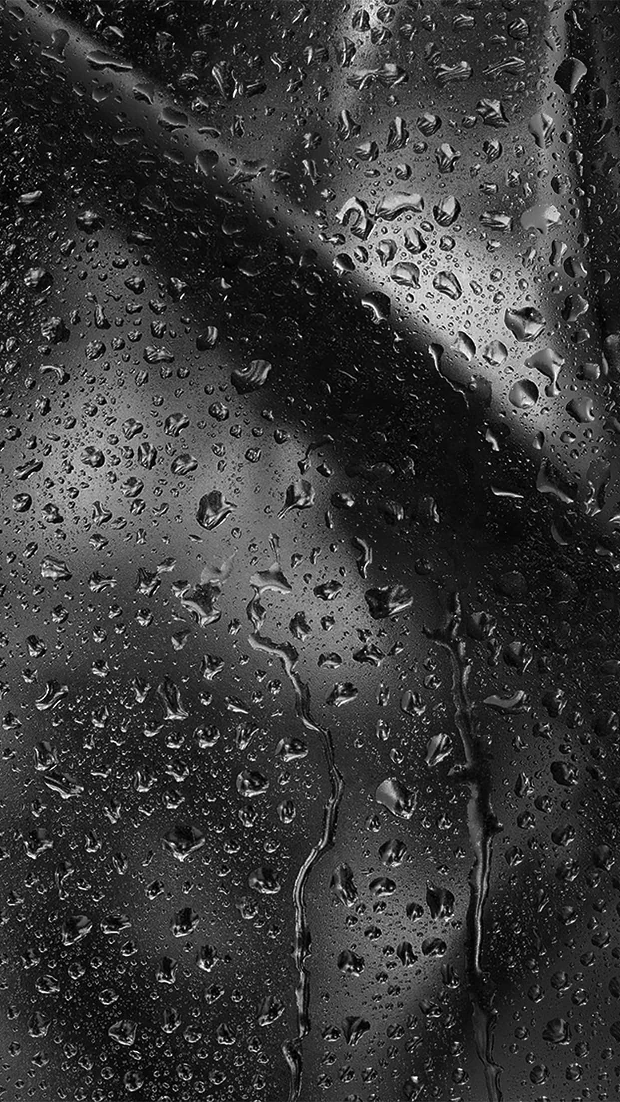 下雨 桌布 壁紙 — 雨滴依附並滑落於深色玻璃表面，反射出單色調中柔和的城市燈光。