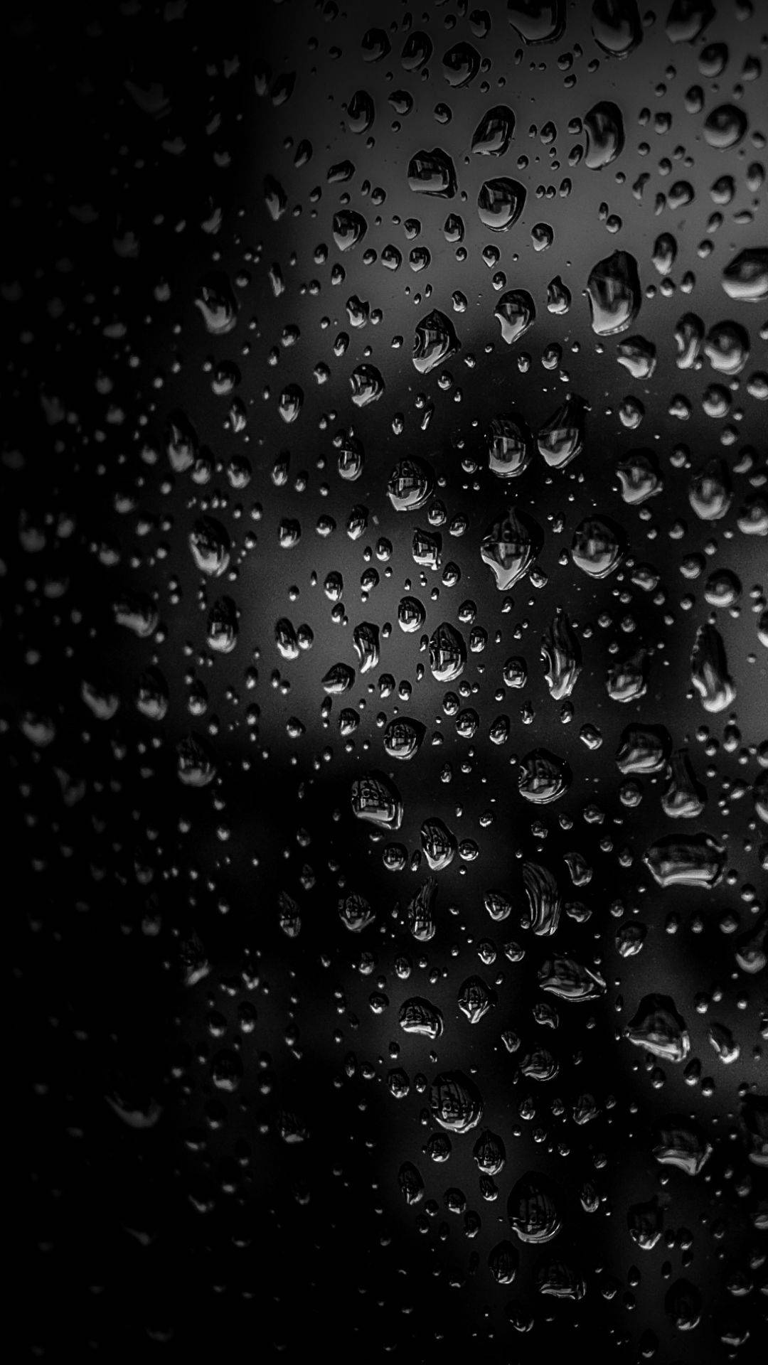 深色玻璃表面上雨滴的特寫，帶有柔和的光線反射。 — 下雨 GIF 壁紙