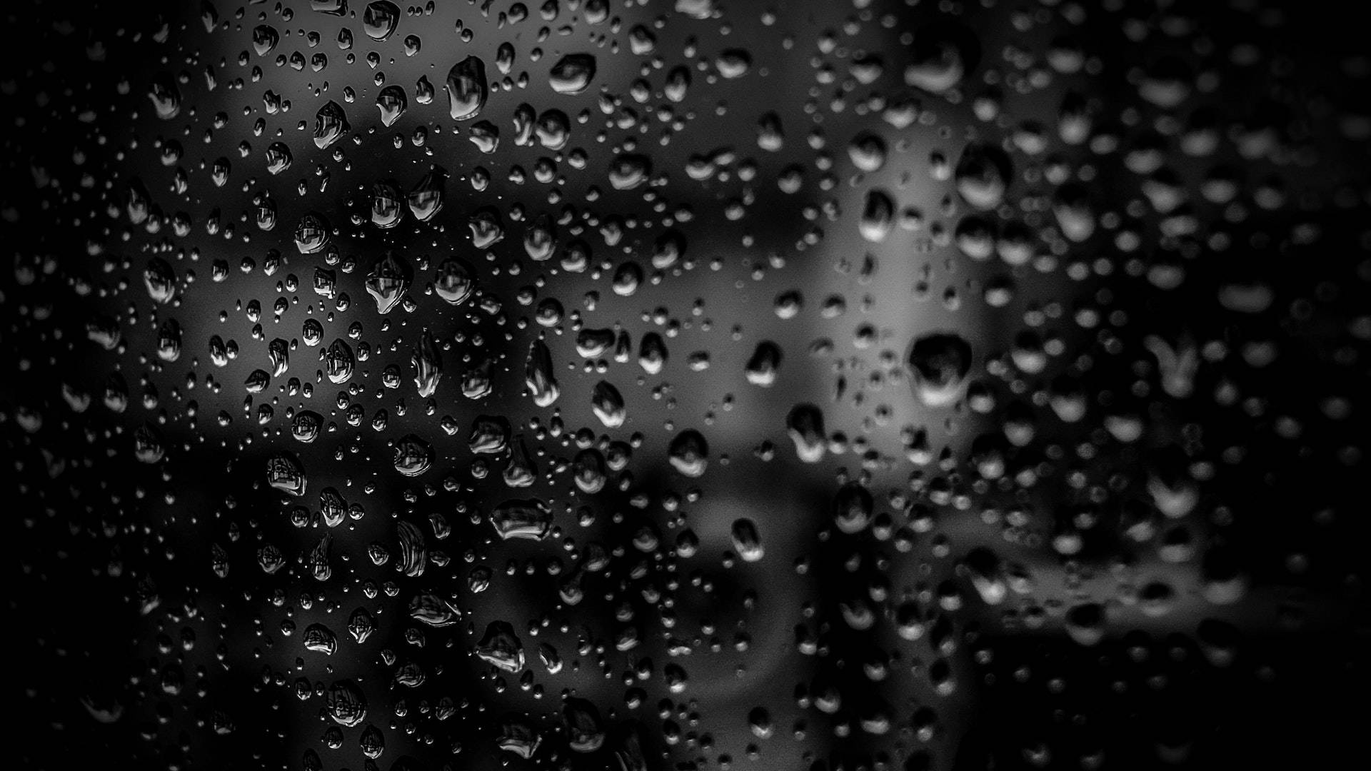 黑色桌面 桌布 壁紙 — 雨滴依附在深色玻璃表面，模糊了背後的單色城市景觀。