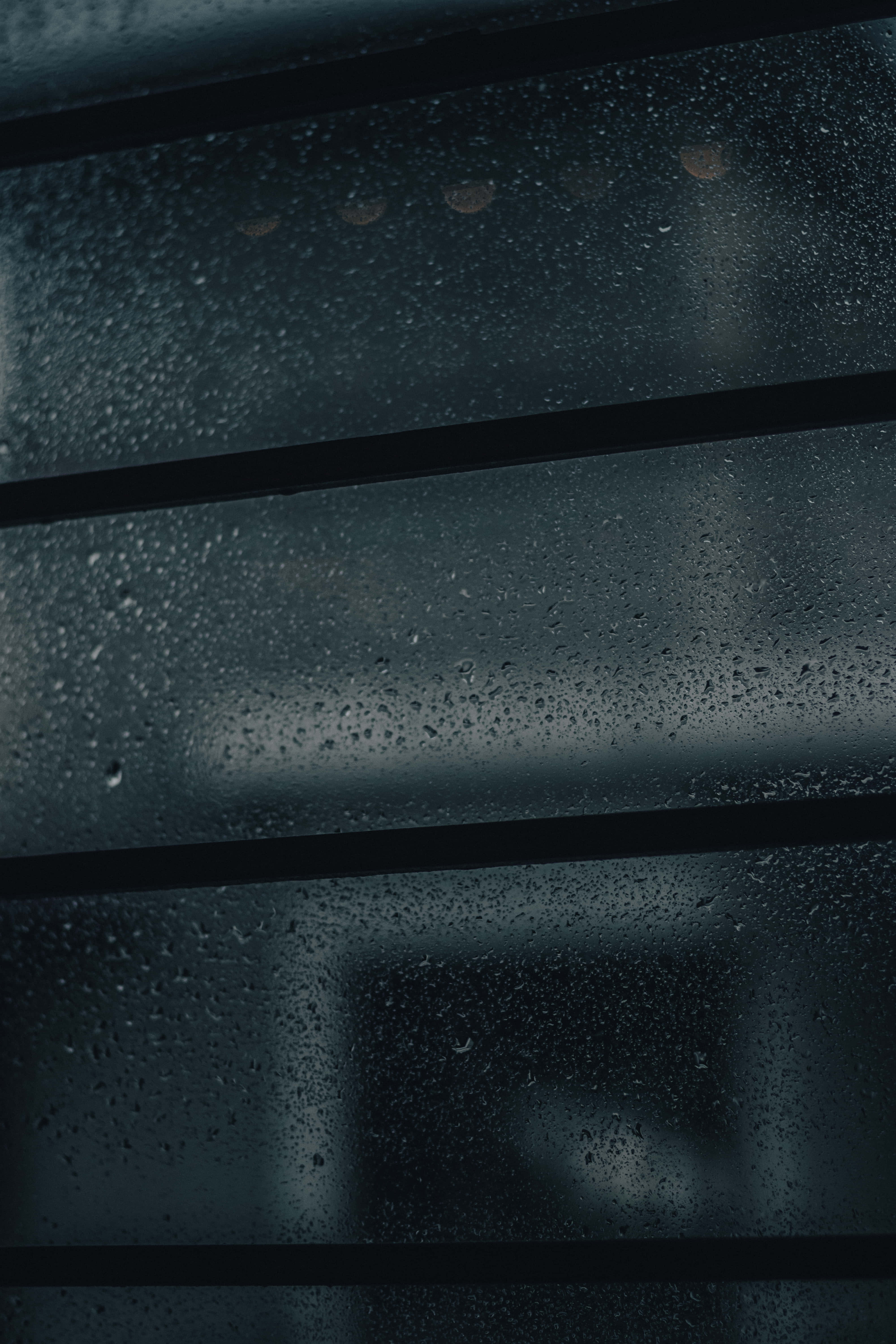 Bad Vibes 桌布 壁紙 — 雨滴依附在深色玻璃表面，由水平條框圍繞，模糊的燈光在遠處可見。