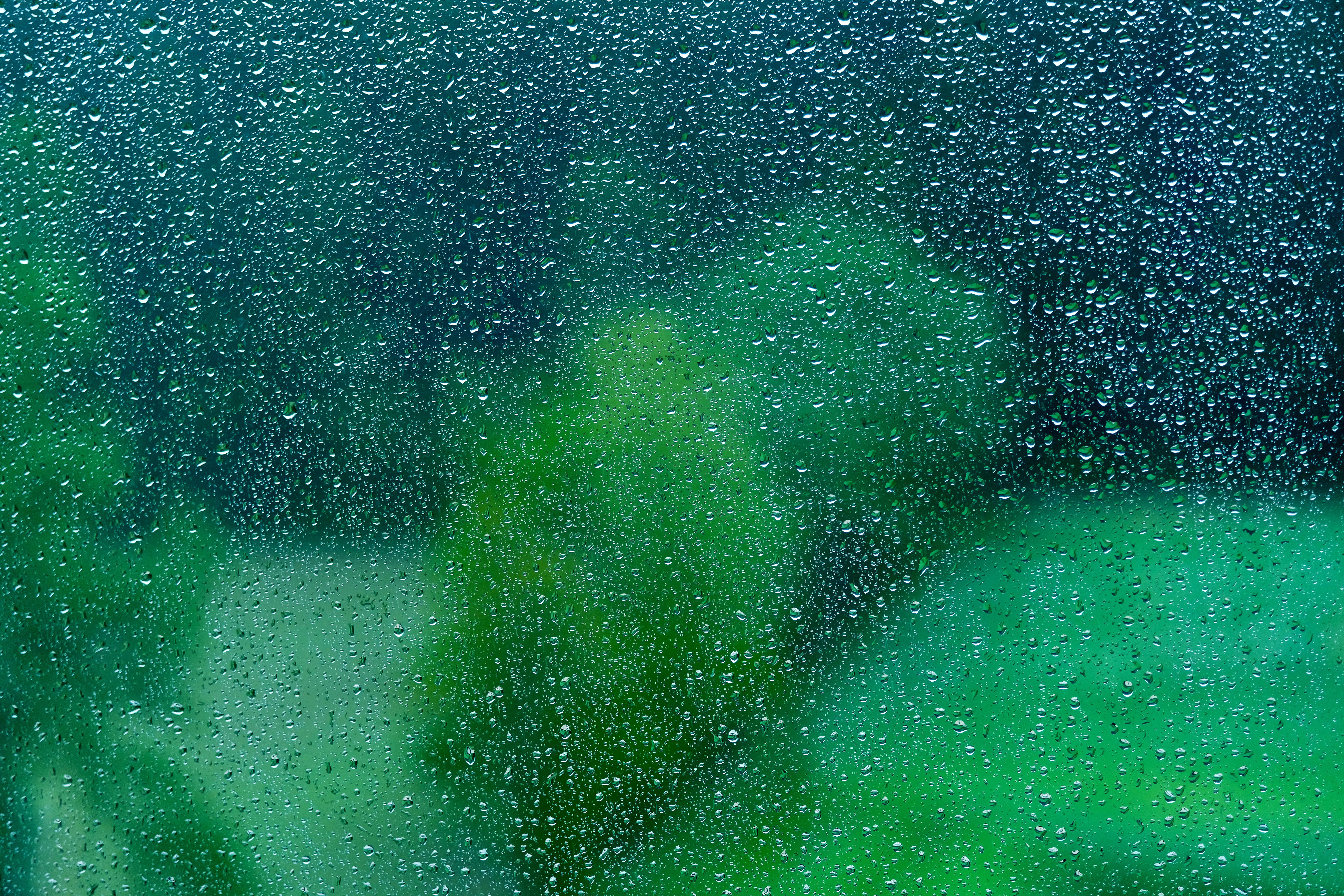 Transparent 桌布 壁紙 — 雨滴依附在玻璃窗上，顯露出窗外模糊的綠色森林，色調清涼。