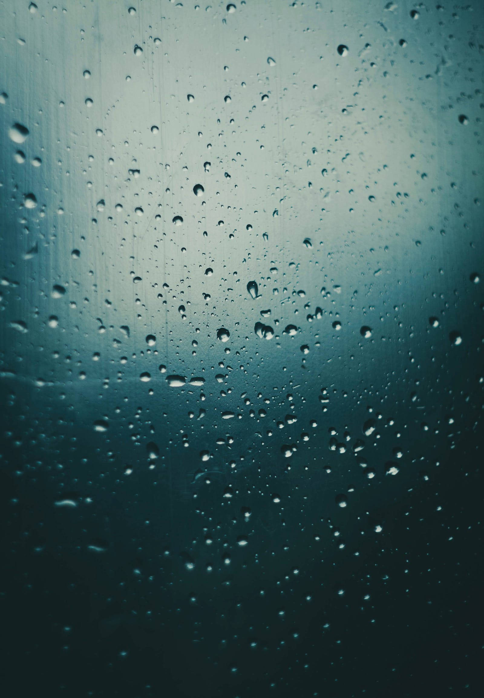 美學藍色 iPhone 桌布 壁紙 — 雨滴依附在玻璃窗上，顯露出窗外模糊的青綠色天空。