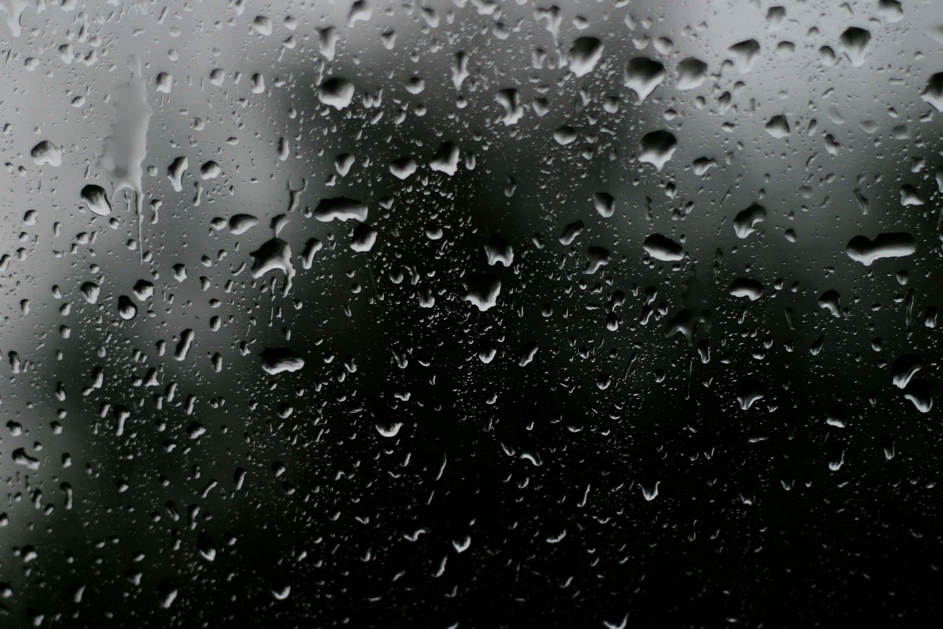 Water Texture 桌布 壁紙 — 雨滴依附在玻璃表面，將黑暗的戶外場景模糊成柔和的灰色調。