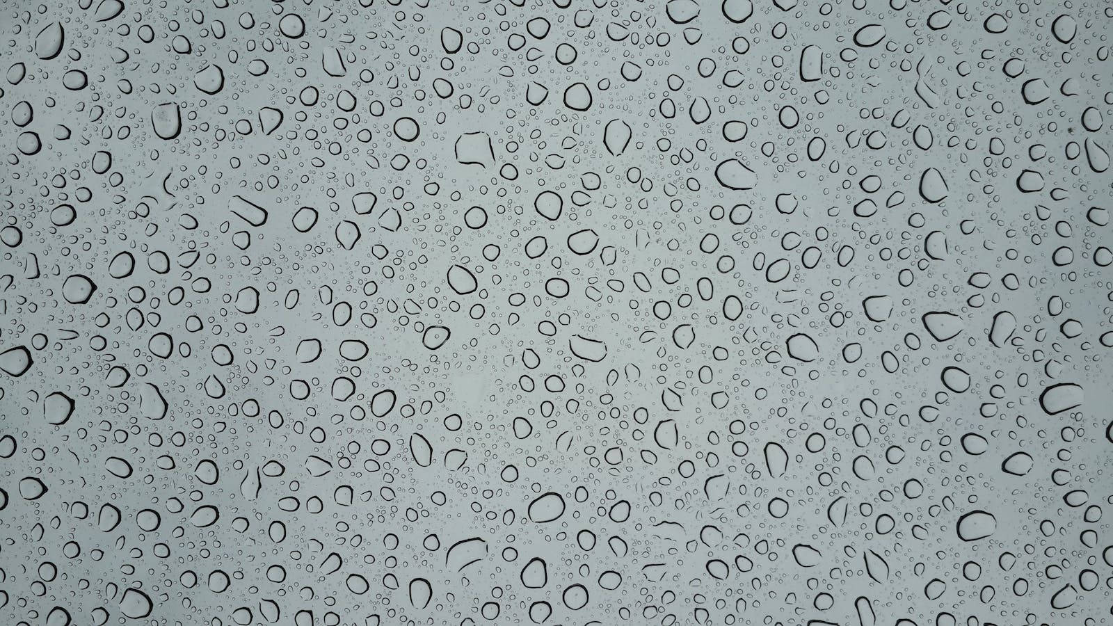 Droplets 桌布 壁紙 — 雨滴依附在玻璃表面，顯露出背後柔和的灰色天空。