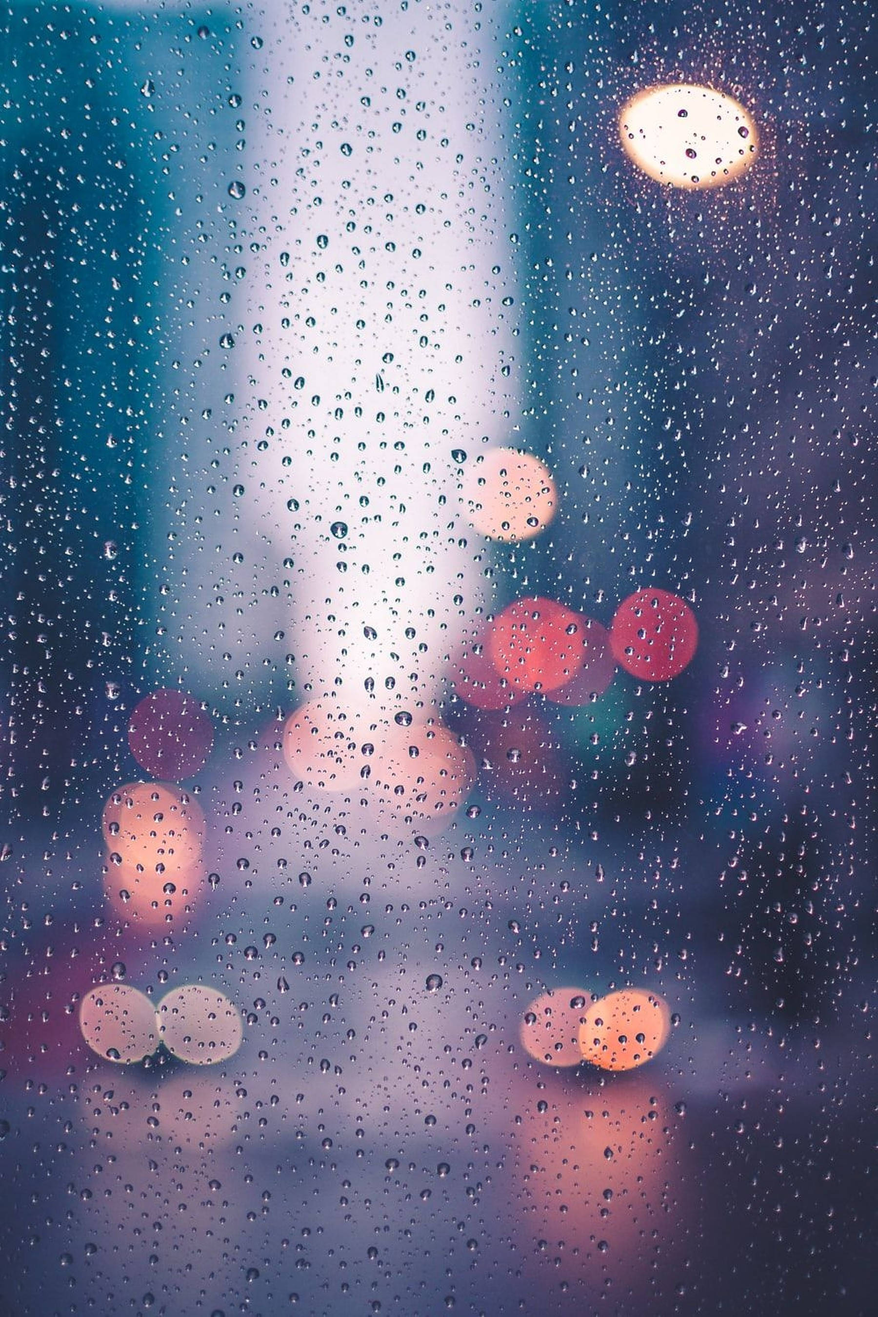 Weather 桌布 壁紙 — 雨滴依附在窗戶上，映出模糊的城市燈光，在清涼的藍色夜晚背景下溫暖地閃爍。