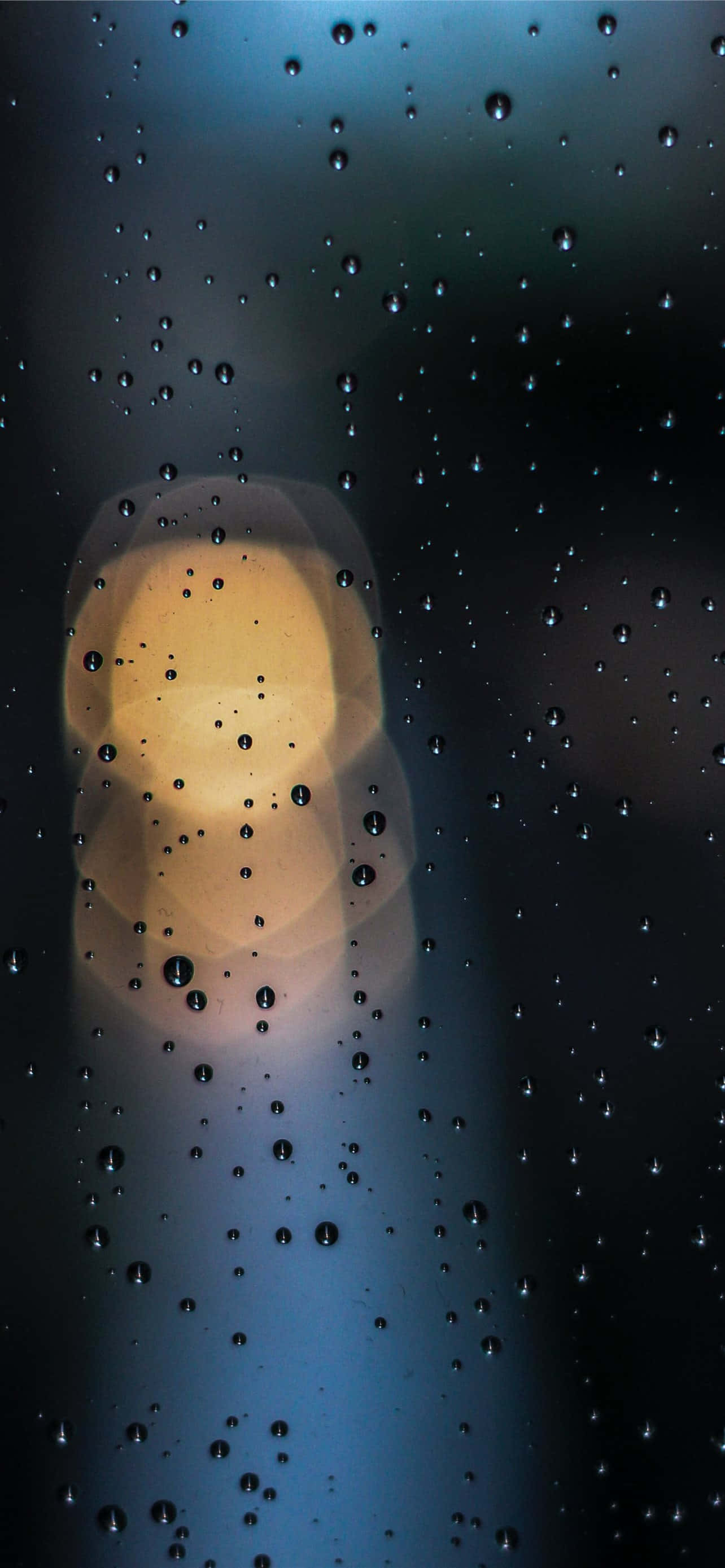 下雨 桌布 壁紙 — 雨滴依附在窗戶上，映出模糊的暖光，背景是清涼的藍色夜空。
