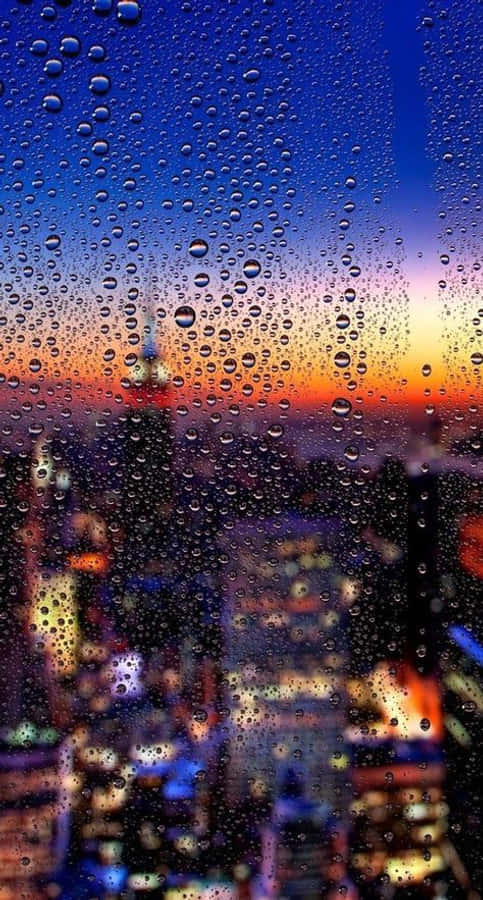 Indefinite 桌布 壁紙 — 雨滴依附在窗戶上，而 vibrant 的日落以橙色和藍色調描繪城市天際線。