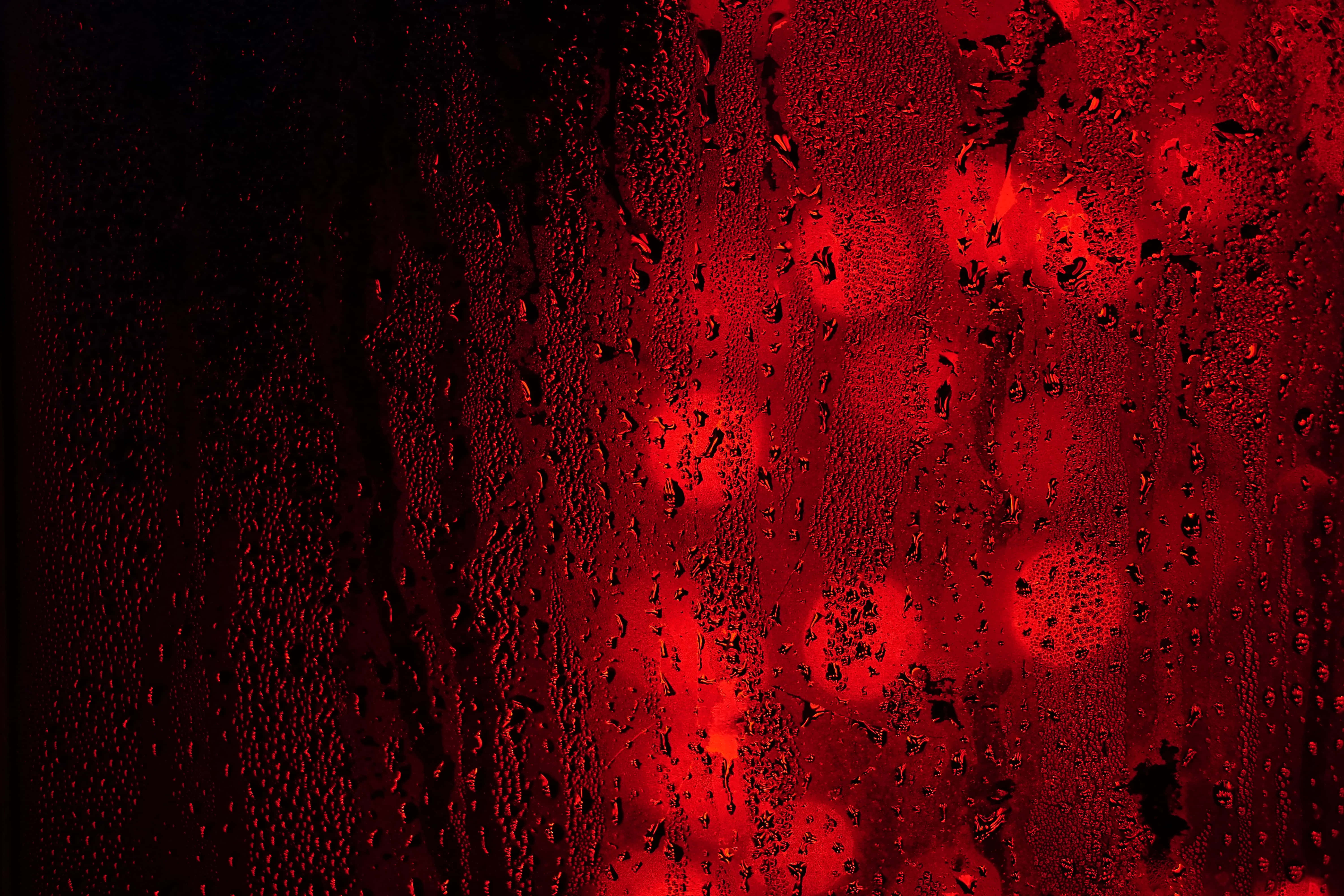 Black And Red 桌布 壁紙 — 雨滴依附在窗戶上，顯露出外面模糊的紅色燈光，營造出憂鬱的夜景。
