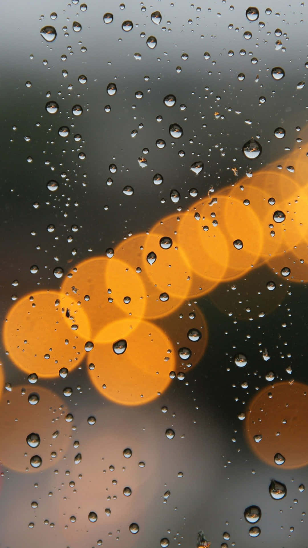 Bokeh 桌布 壁紙 — 雨滴依附在窗戶上，顯露出外面街燈模糊的金色散景燈光。