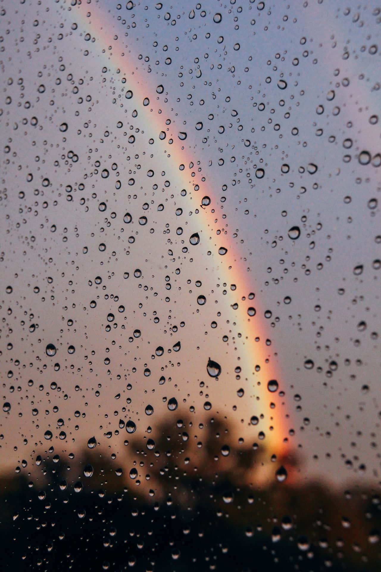 Raindrops 桌布 壁紙 — 雨滴依附在窗戶上，顯露出柔和的彩虹在暮色雲層中發光。