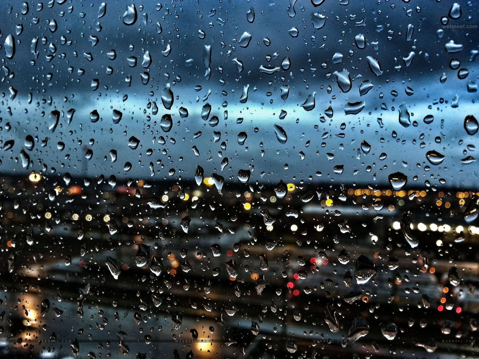 下雨 桌布 壁紙 — 雨滴依附在窗戶上，顯露出模糊的城市景觀，在憂鬱的暮色天空下閃爍著溫暖的燈光。