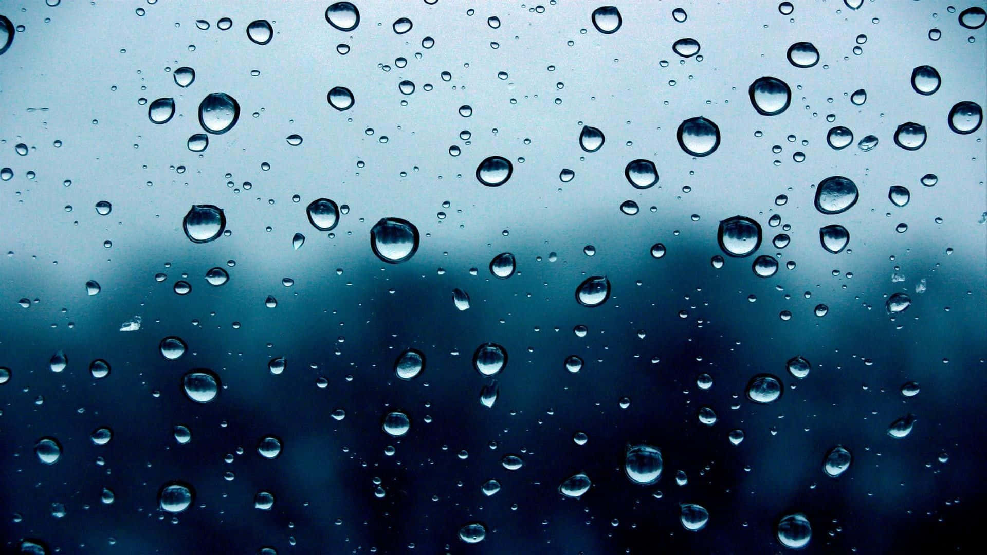 桌布 壁紙 — 雨滴依附在窗戶上，顯露出模糊的藍灰色天空和遠處的樹木，呈現柔焦效果。